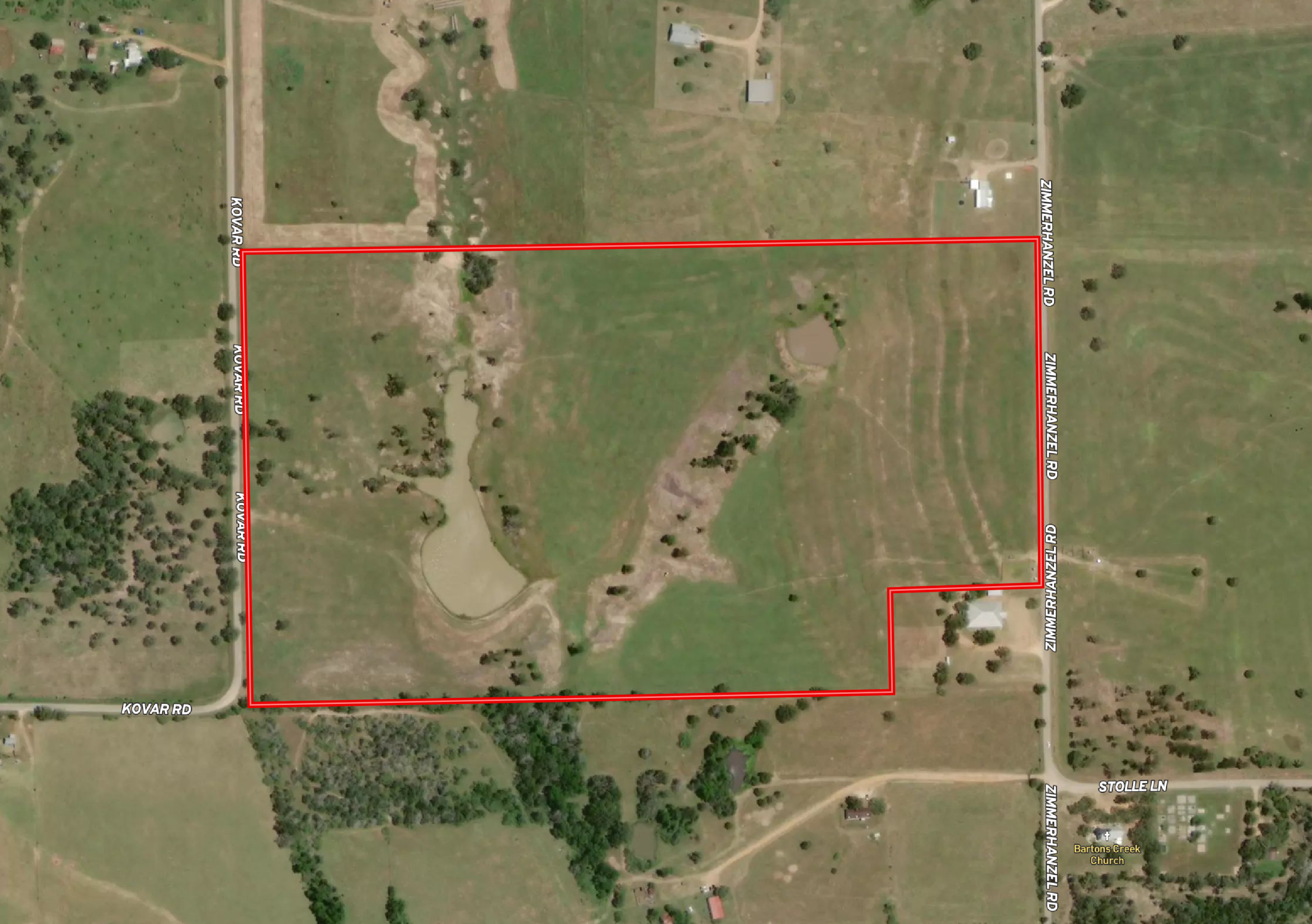 A satellite view of a rural area with a large rectangular plot outlined in red, surrounded by roads, buildings, and open fields.