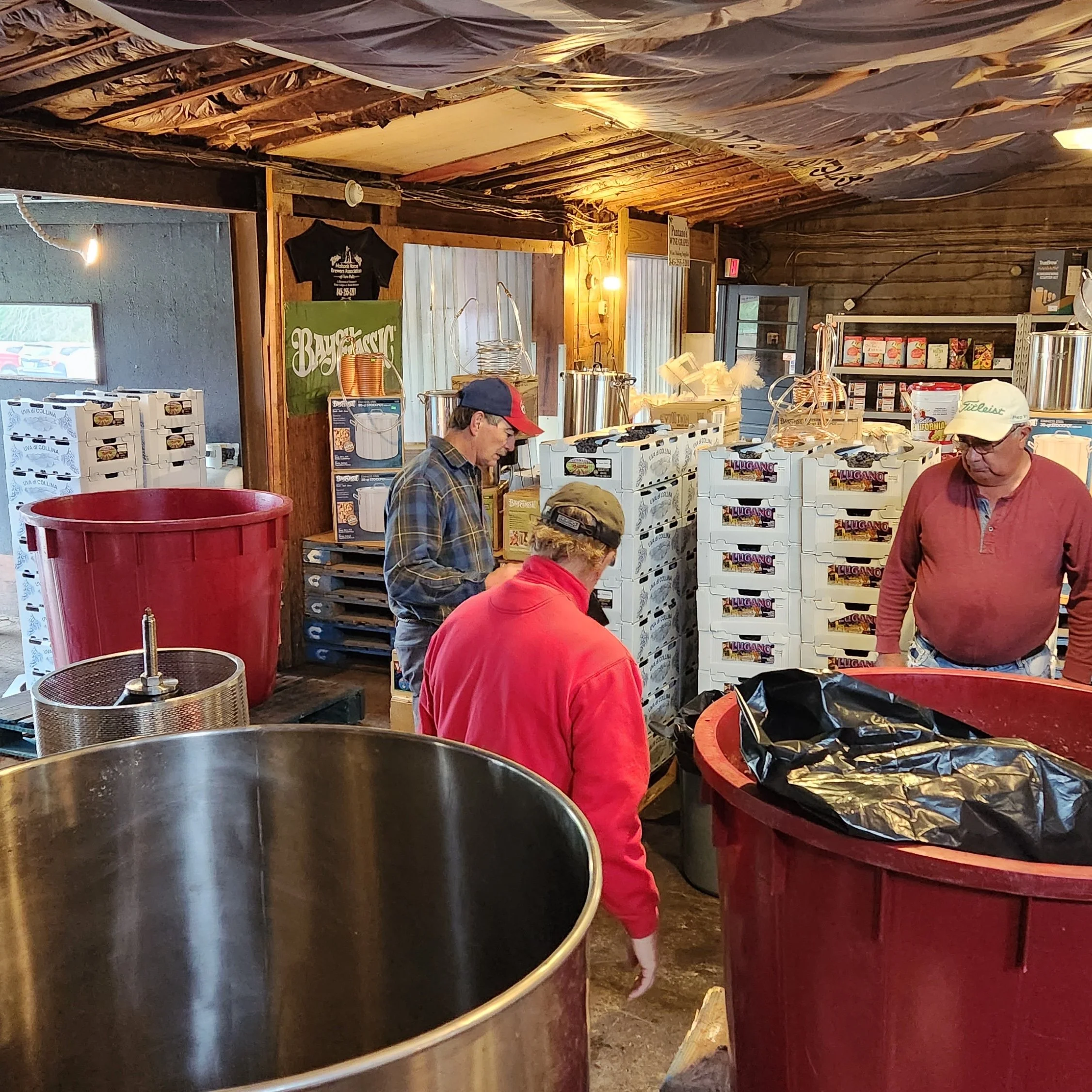 People at a market stall with boxes of fresh produce, large metal containers, and colorful indoor decor.
