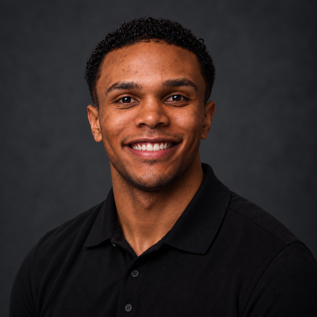 A smiling young man with curly black hair, wearing a black shirt, against a dark gray background.
