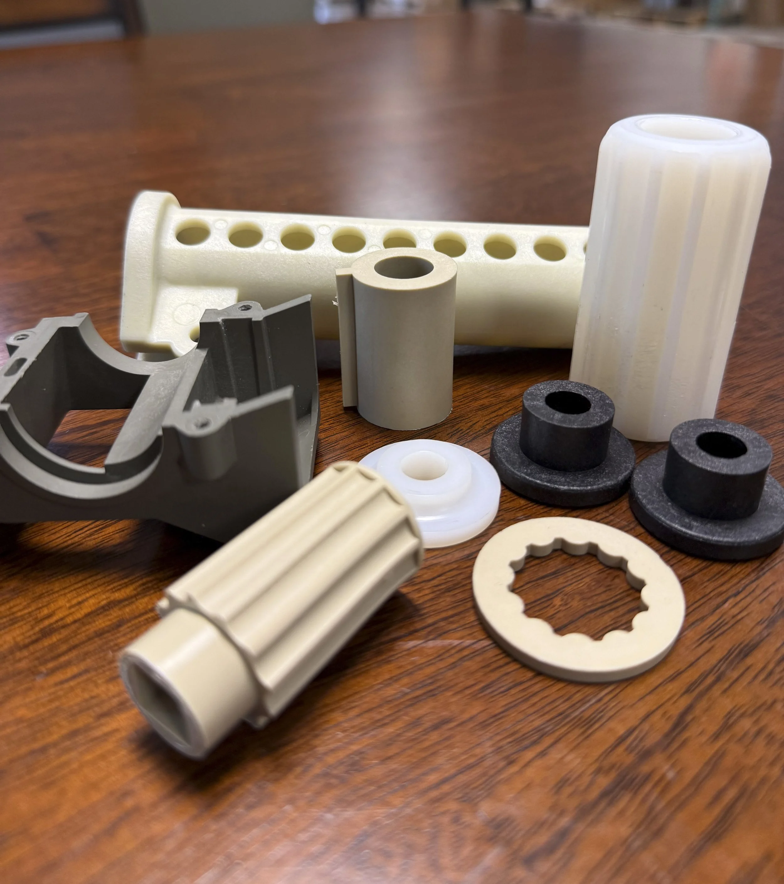 Various plastic and rubber parts on a wooden surface, including cylindrical, ring-shaped, and uniquely shaped pieces in white, gray, and black colors.