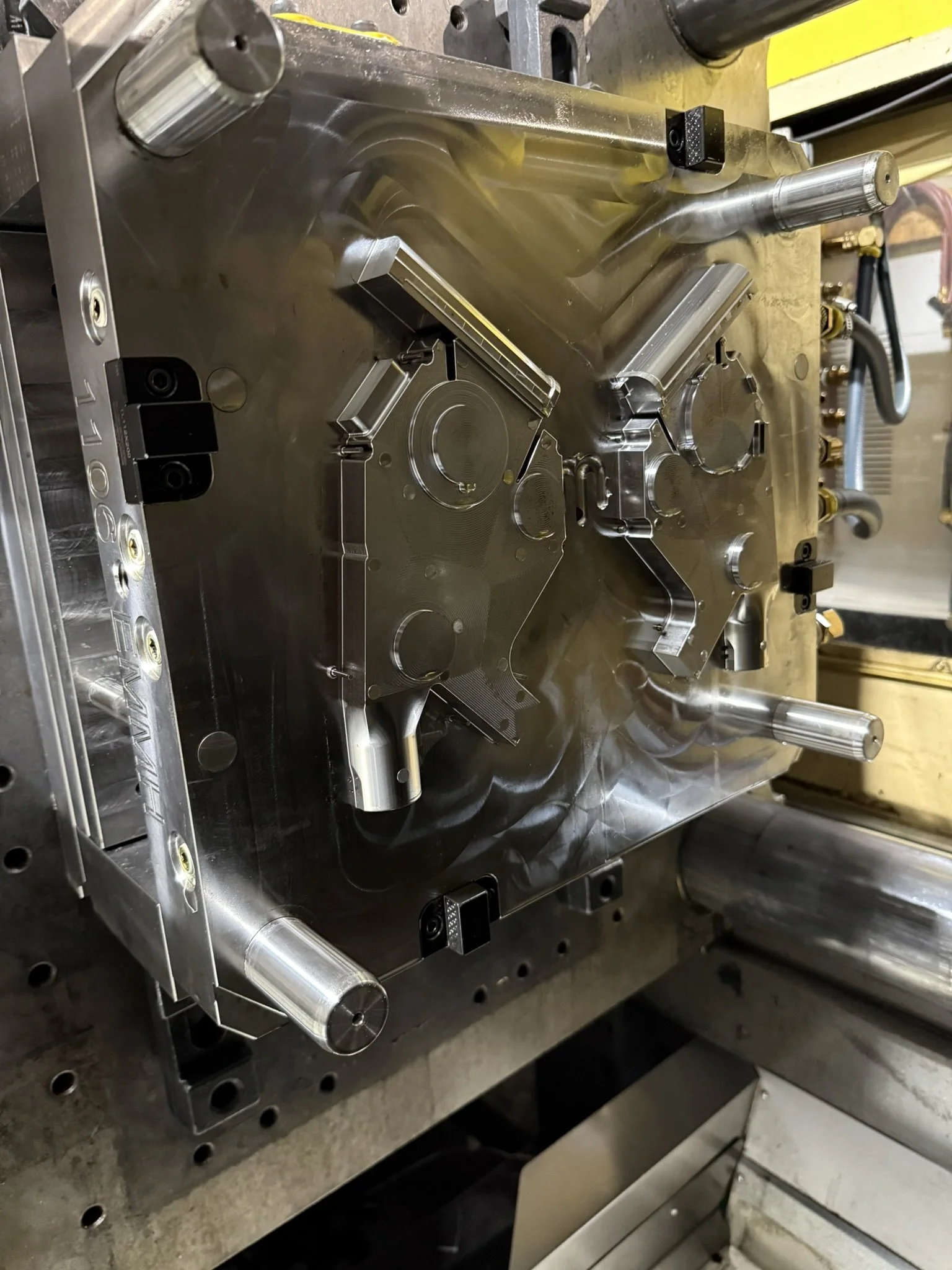 Close-up of a metal mold used in manufacturing, with cylindrical and rectangular components, resting on a workbench.
