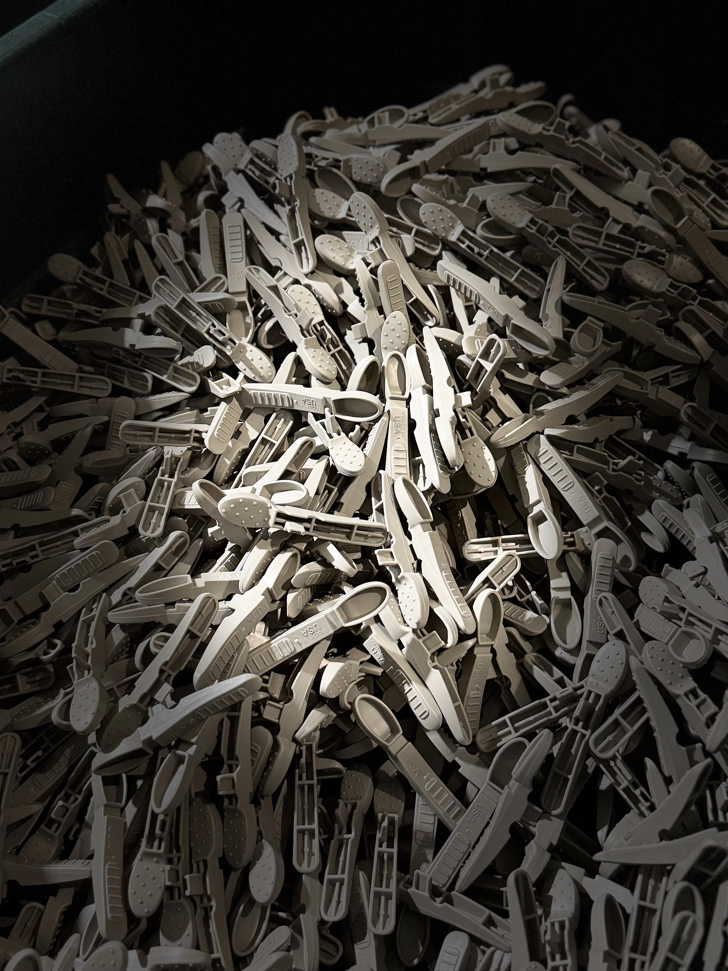 A large pile of white plastic shoehorns in a dark bin.