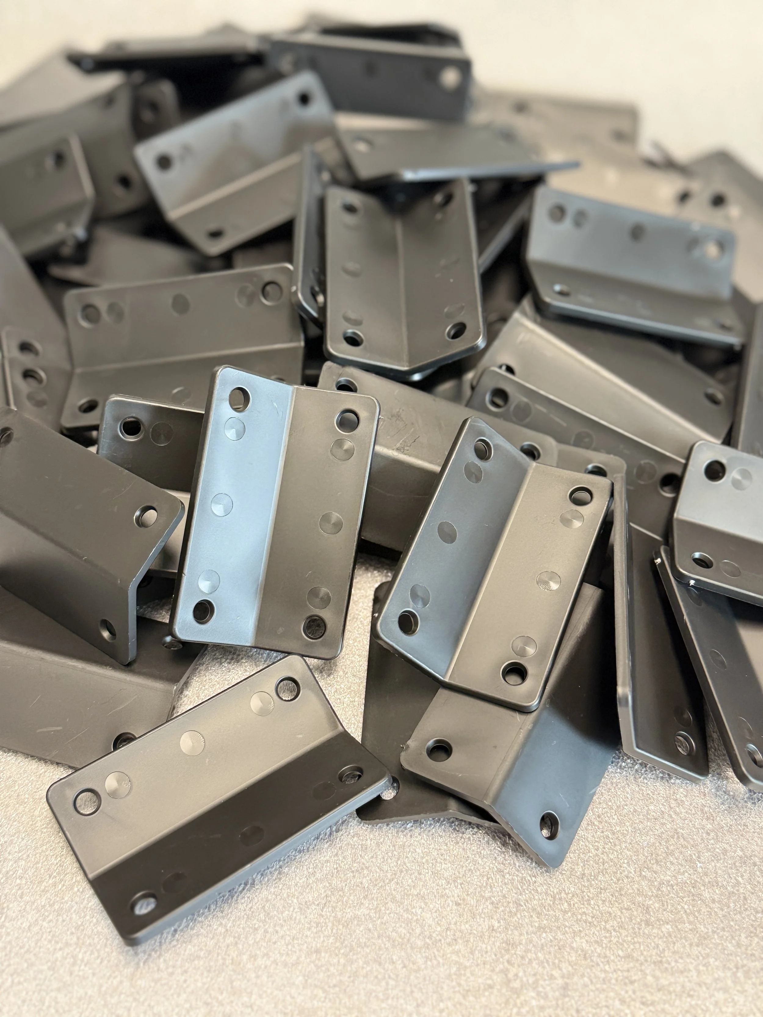 A pile of metal L-shaped brackets with multiple holes, stacked on a metallic surface.
