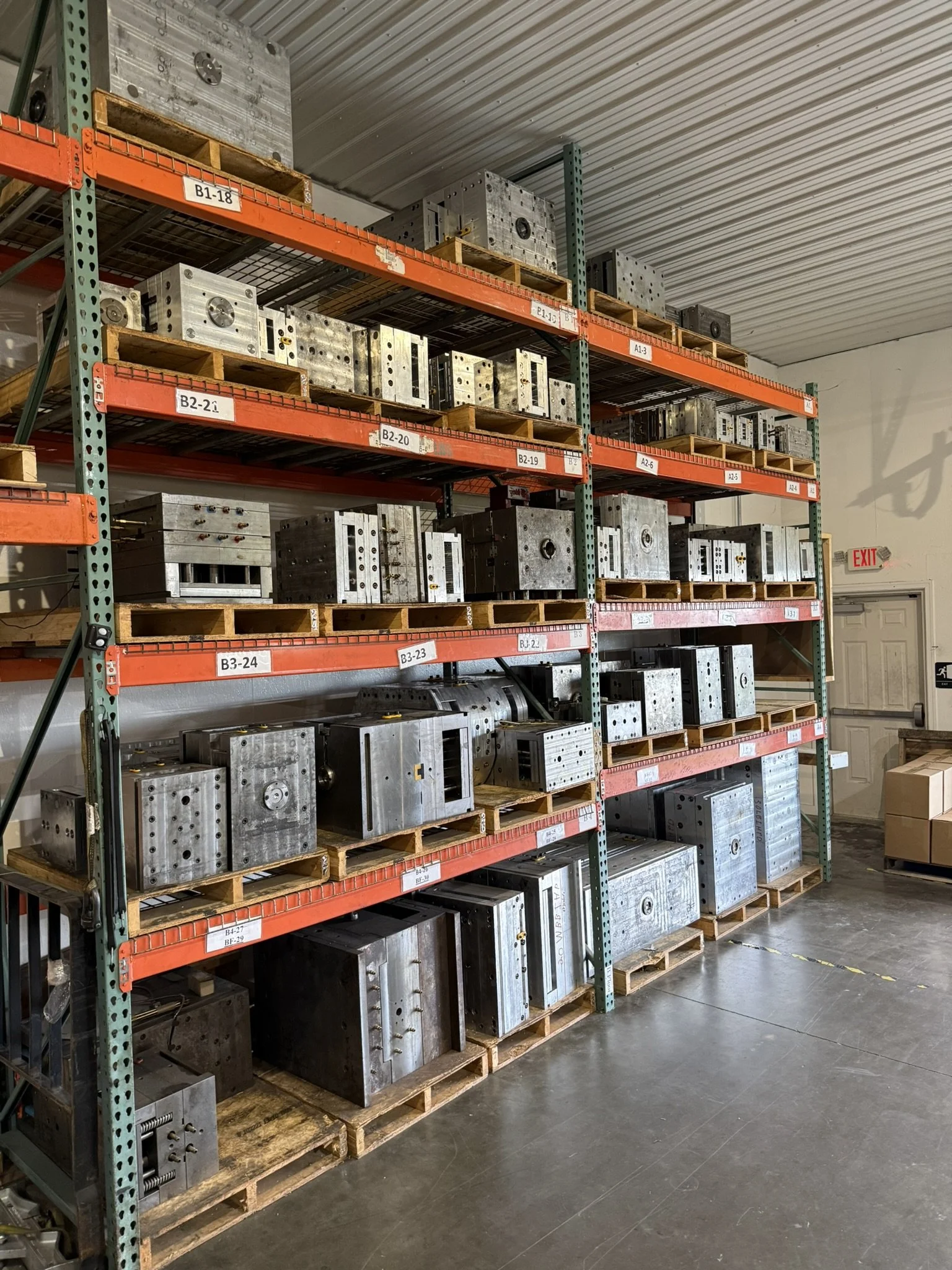 Metal molds stored on warehouse shelves with labeled sections.