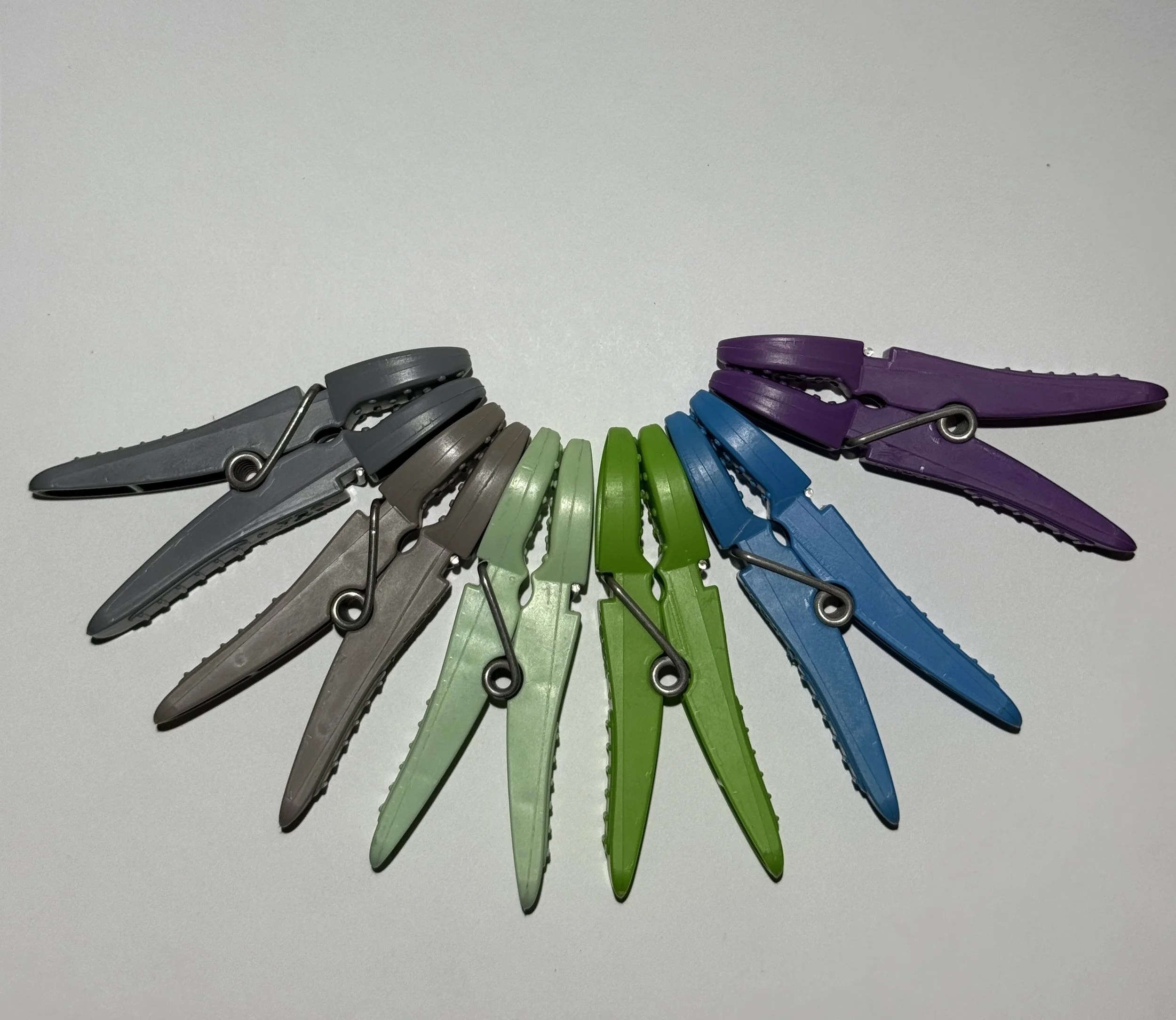 A circular arrangement of colorful clothespins in shades of gray, green, blue, and purple on a white background.
