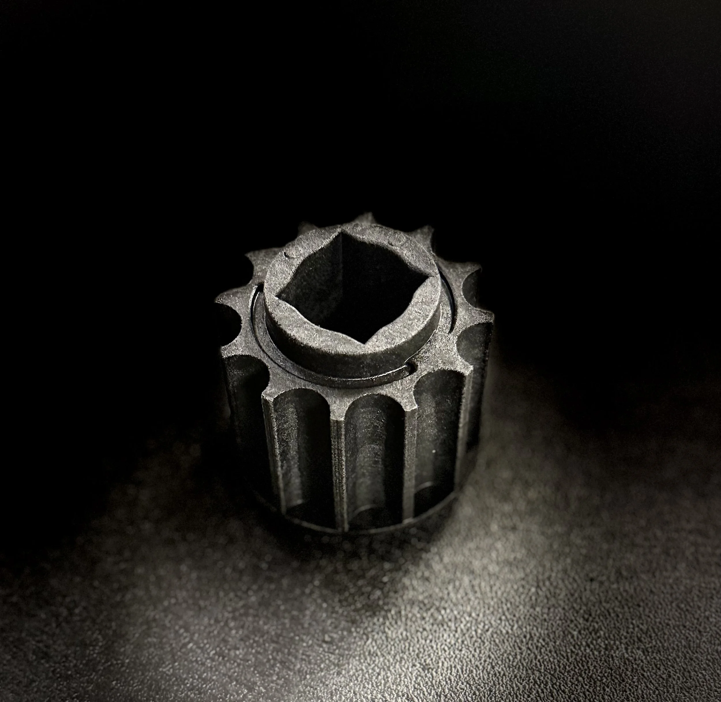 Close-up of a metallic gear or cogwheel with a dark background and textured surface.