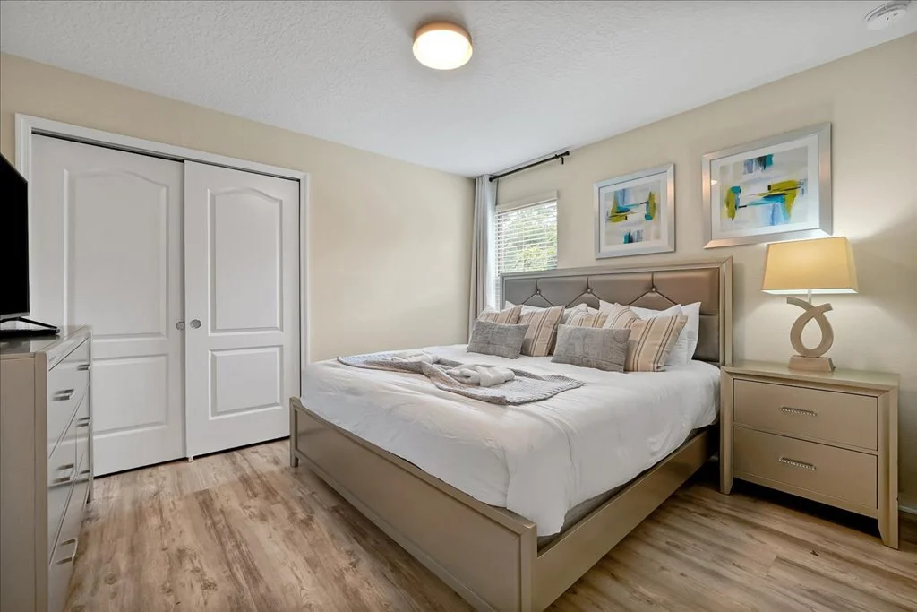A bedroom with a beige bed, nightstand, dresser, and abstract artwork on the wall.