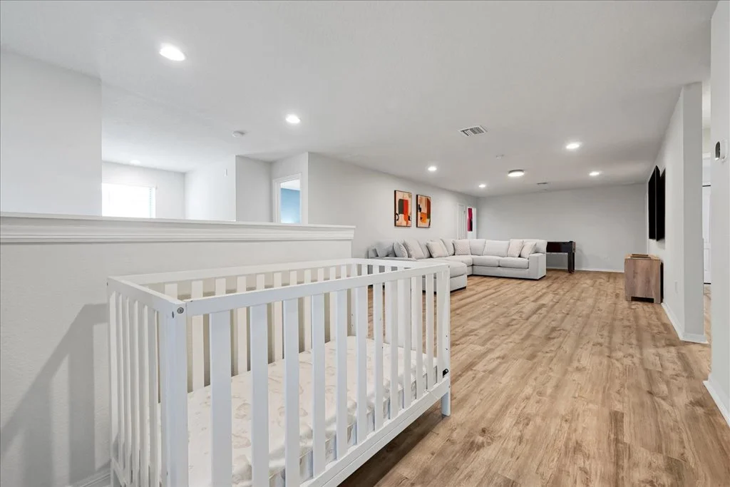 Empty nursery with white crib and spacious living room with large sectional sofa and framed art on the wall.