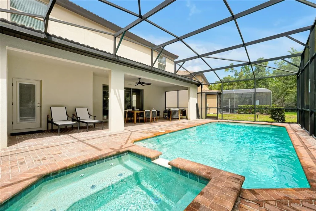 Backyard with screened-in patio area containing a pool and hot tub, patio furniture, and surrounding greenery.