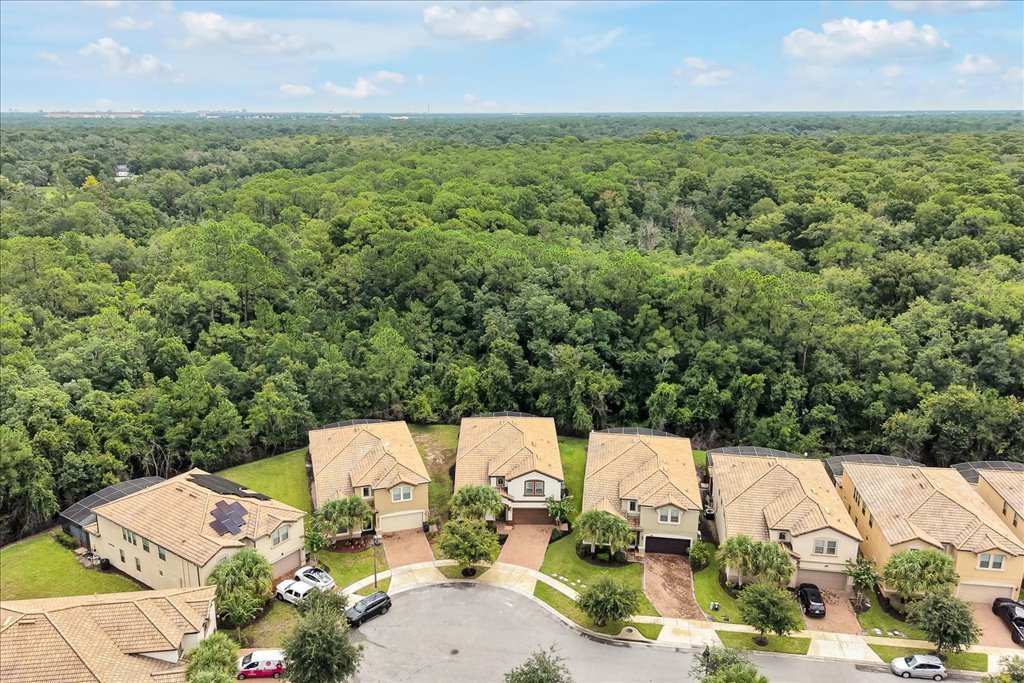 Aerial view of a the neighborhood surrounded by a dense forest, under a partly cloudy sky.