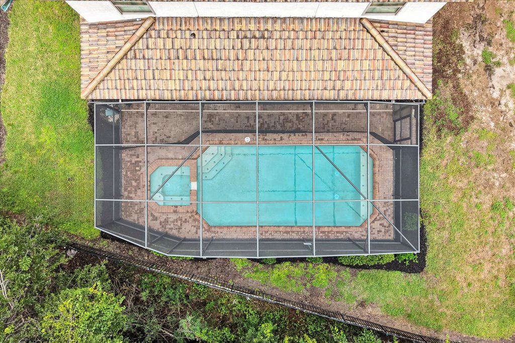 A screened-in backyard pool enclosure surrounding a blue swimming pool with built-in stairs, located next to a house with a tiled roof.