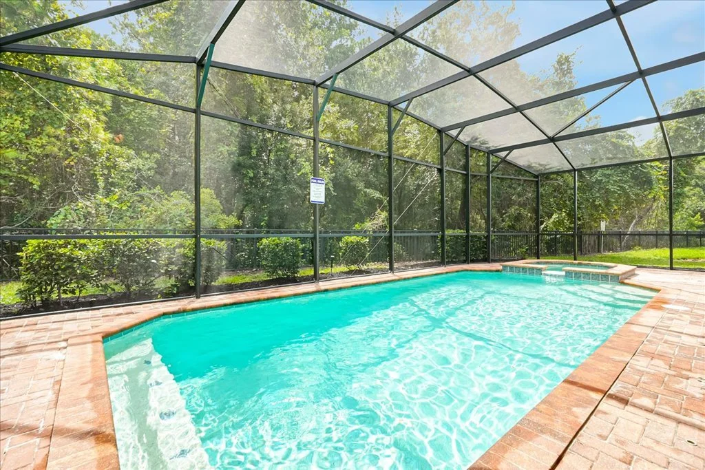 Heated outdoor swimming pool surrounded by a paved deck enclosed by a black screened fence facing a conservation area