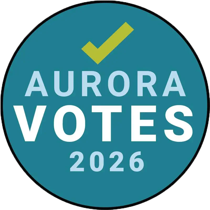 A circular badge with a teal background and a yellow check mark at the top. The text reads "Aurora Votes 2026."