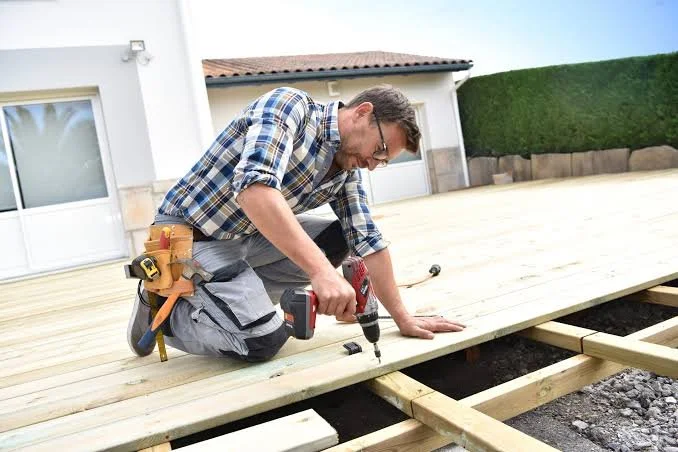 Man installing a wooden deck using a cordless drill outdoors.