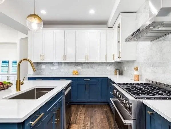 Modern kitchen with white upper cabinets, blue lower cabinets, white countertop, stainless steel stove, and gold fixtures.