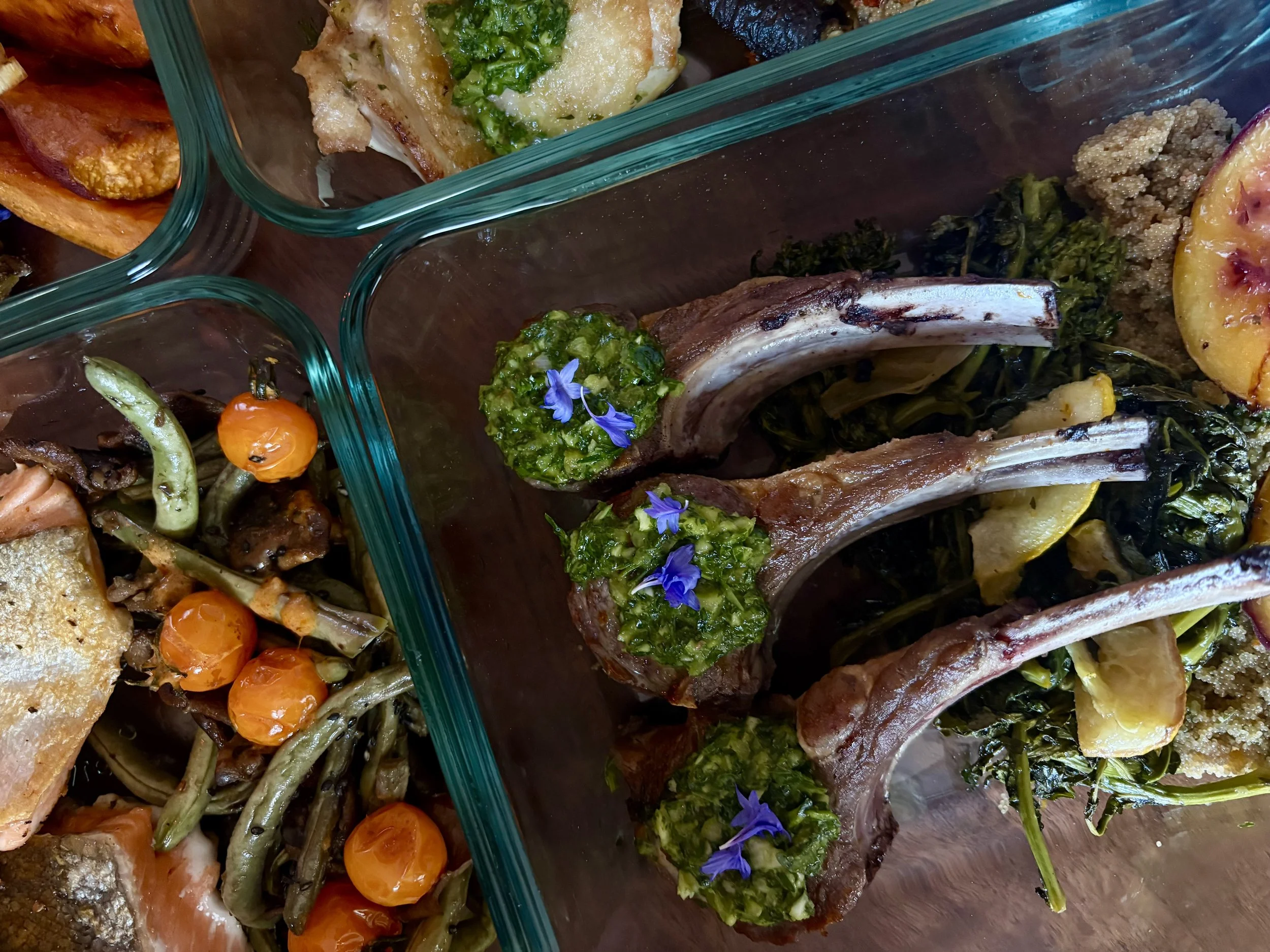Glass container with lamb chops and sauce, edible flowers, some vegetables