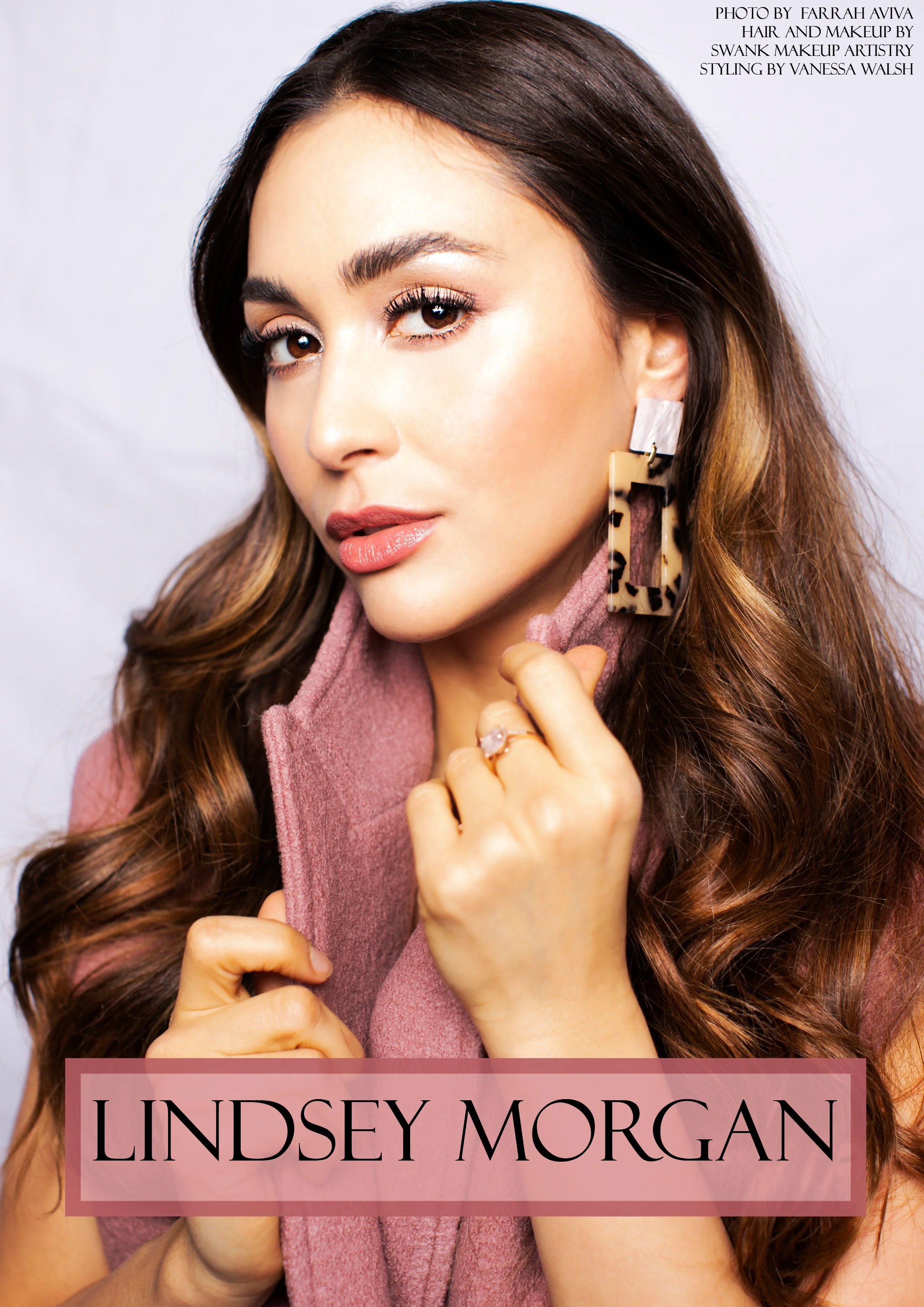 Close-up portrait of a woman with brown hair and tan skin, wearing makeup, a pink scarf, a large geometric earring, and a ring on her finger, with text overlay reading 'Lindsey Morgan'.
