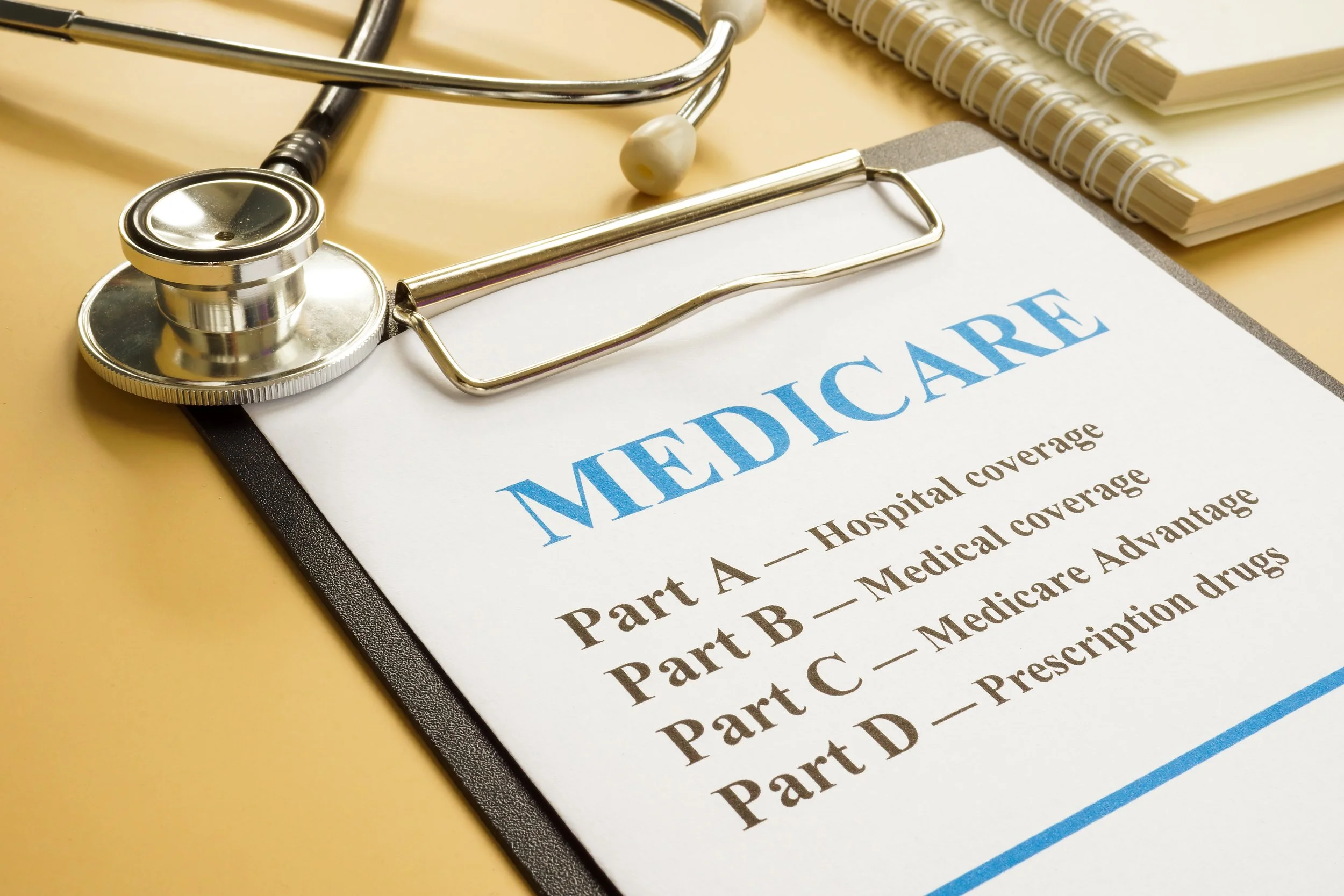 Close-up of a stethoscope, notepad, and a contract titled 'MEDICARE' on a yellow surface.