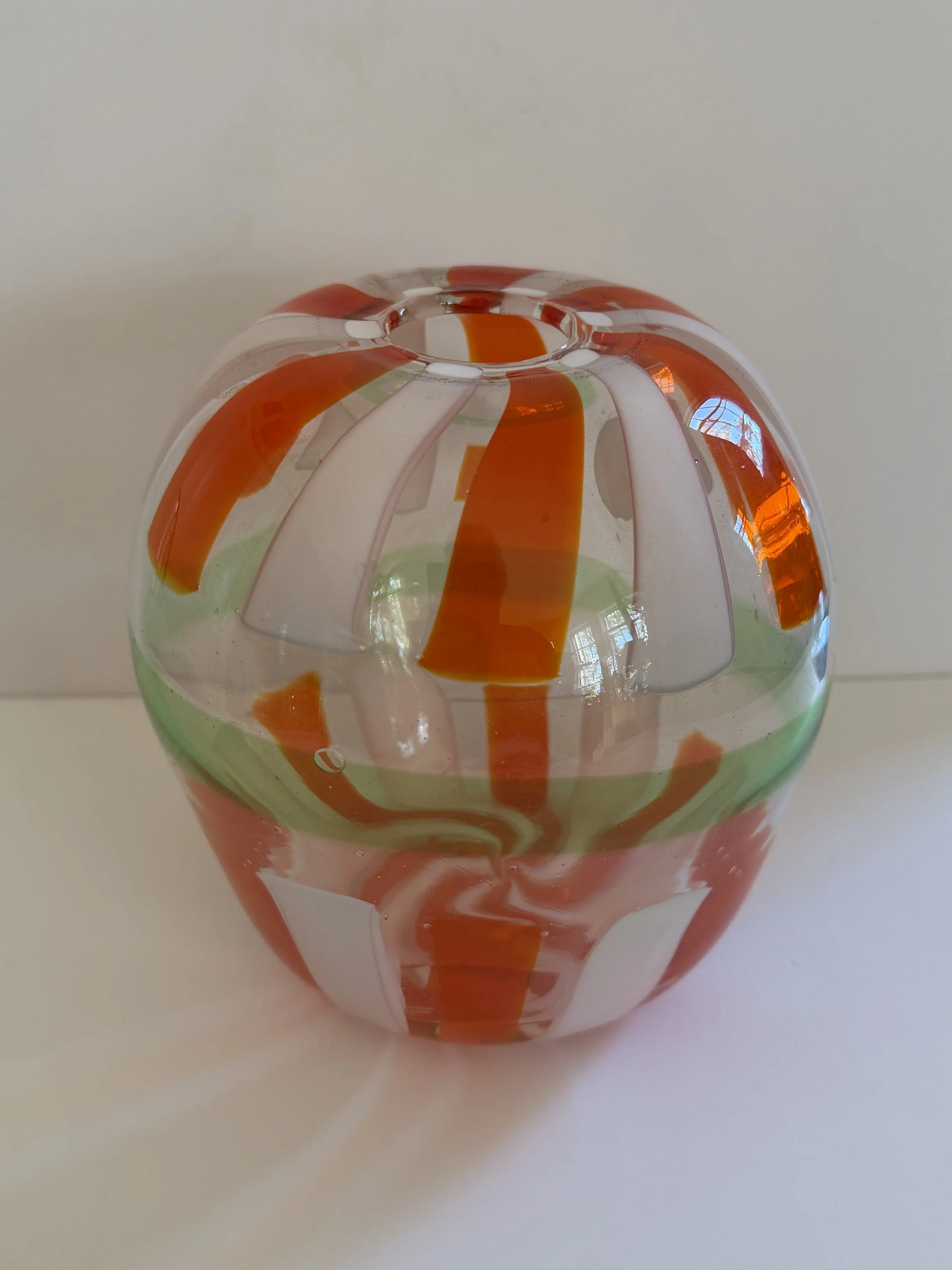Handblown glass vase: Clear, pumpkin-shaped with orange stripes and a green belt.