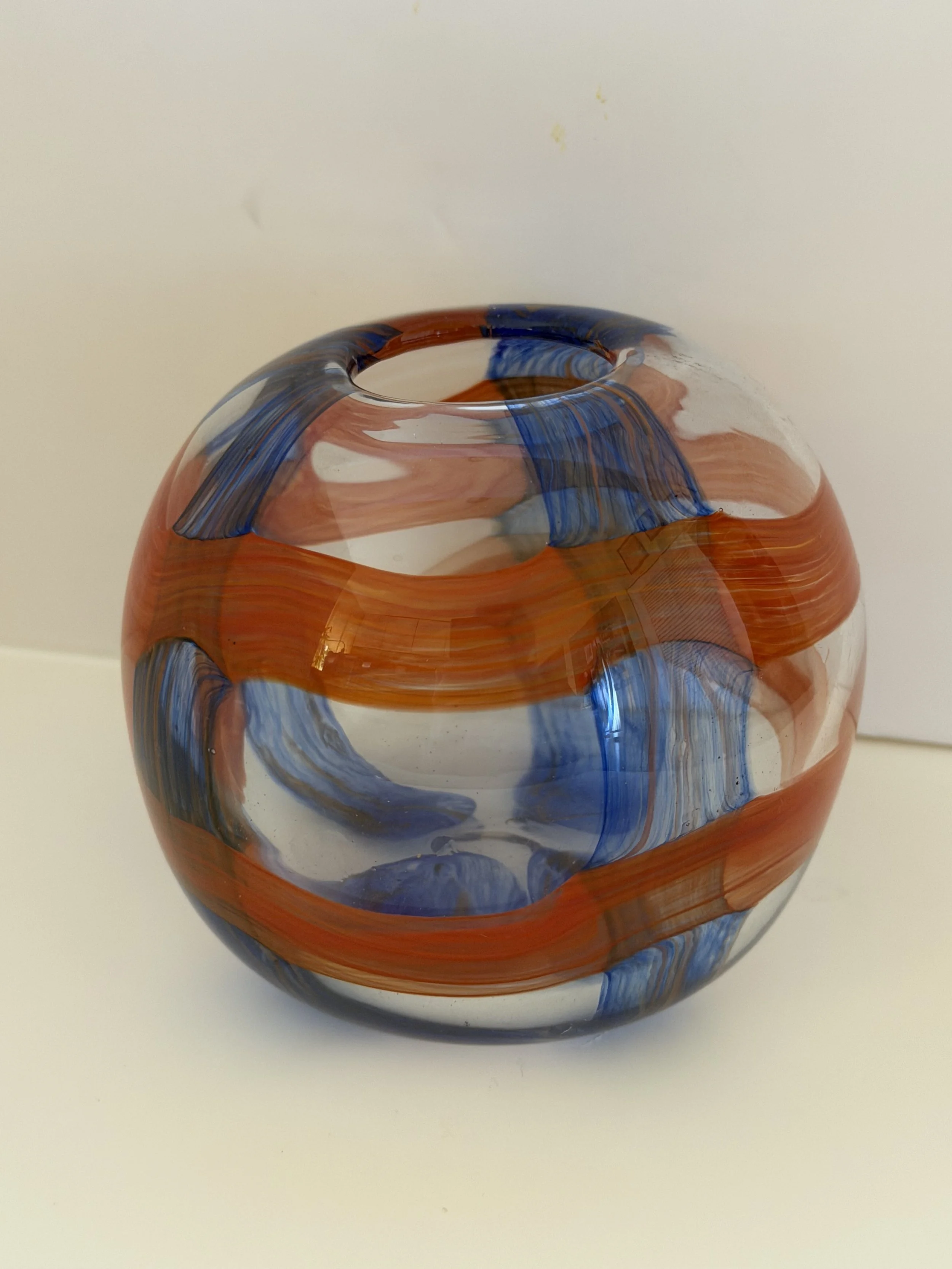 Small clear handblown glass globe with textured red and blue checkerboard bands.