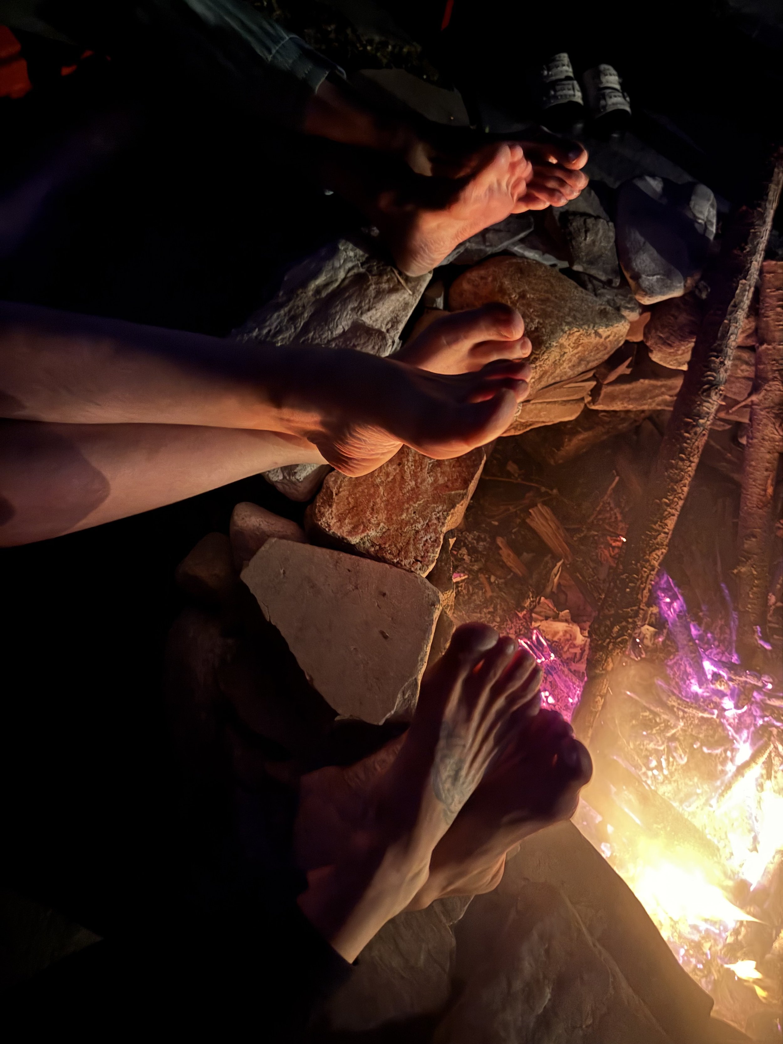 People sitting around a campfire, with their hands extended towards the flames, at night.