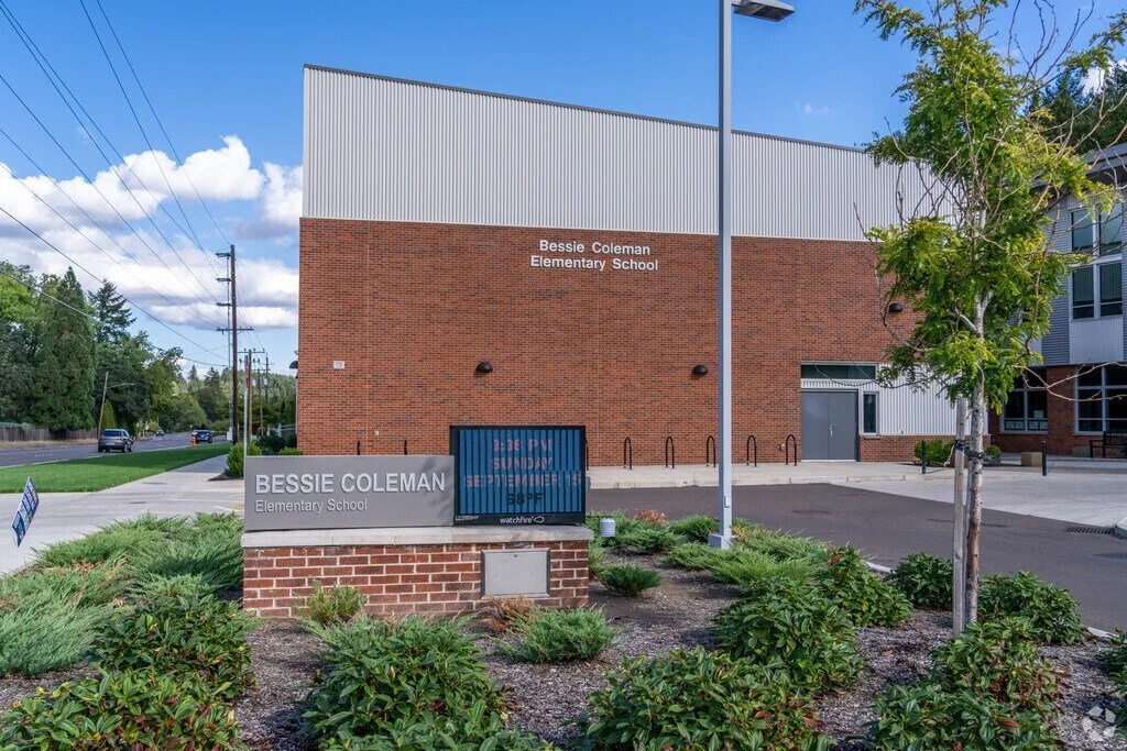Front view of Bessie Coleman Elementary School with a brick building, a sign, and landscaped garden in the foreground.