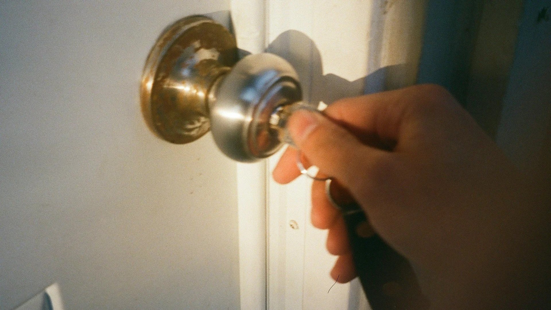 A person turning a brass doorknob on a white door.