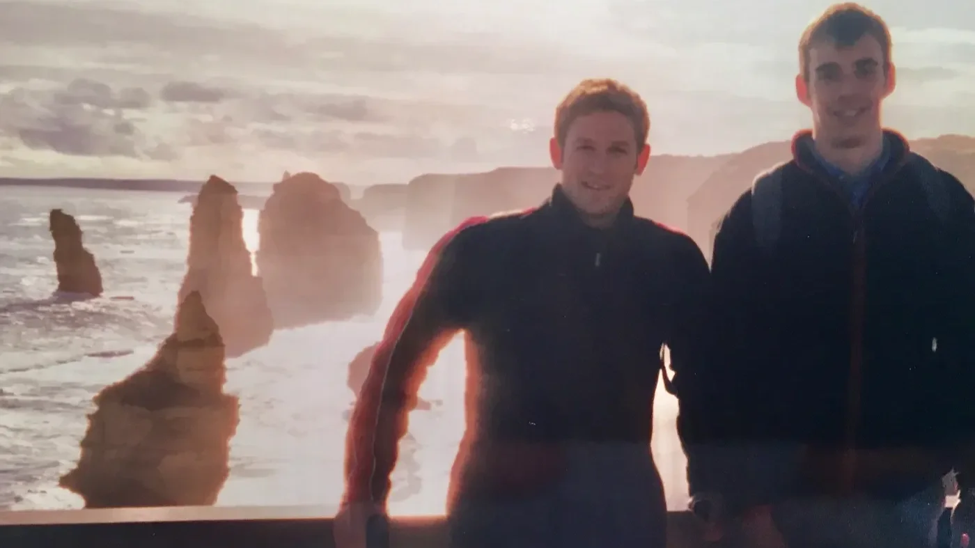Two young men standing on the coast in Australia with sea stacks and rocky formations in the background during sunset, which are the famed Seven Sisters.