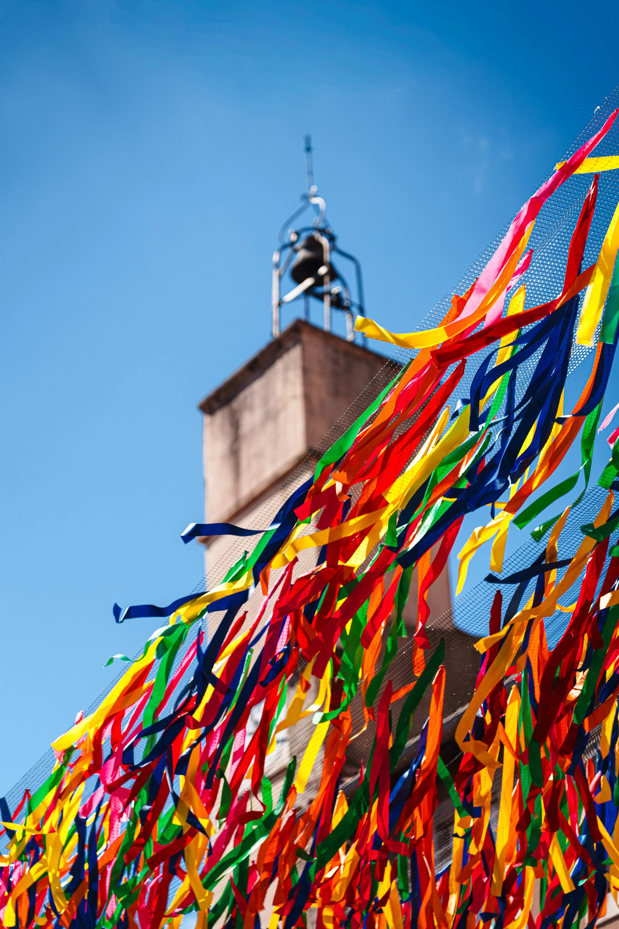 Colorful streamers hanging on a fence in front of a building with a chimney, against a clear blue sky.