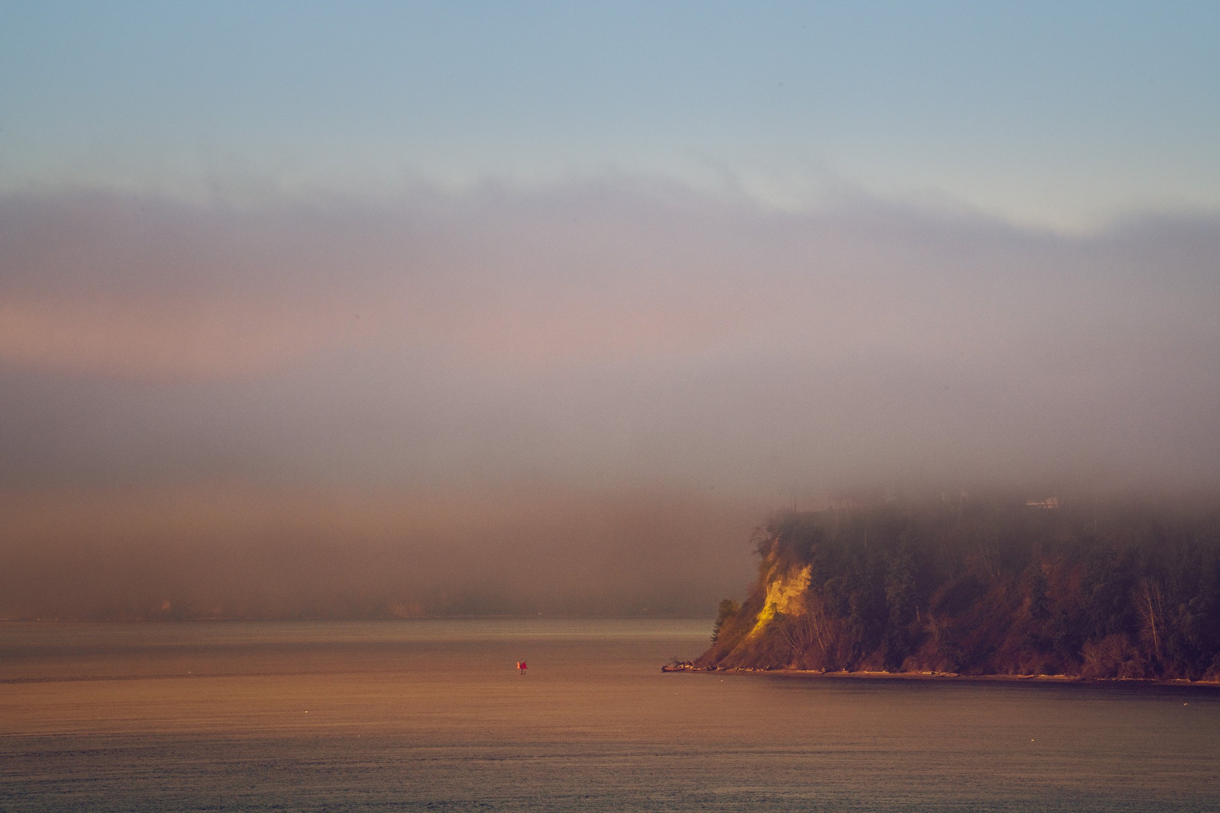 Overcast sky with a distant cliff on the right side, ocean in the foreground, and a small red boat near the shore.