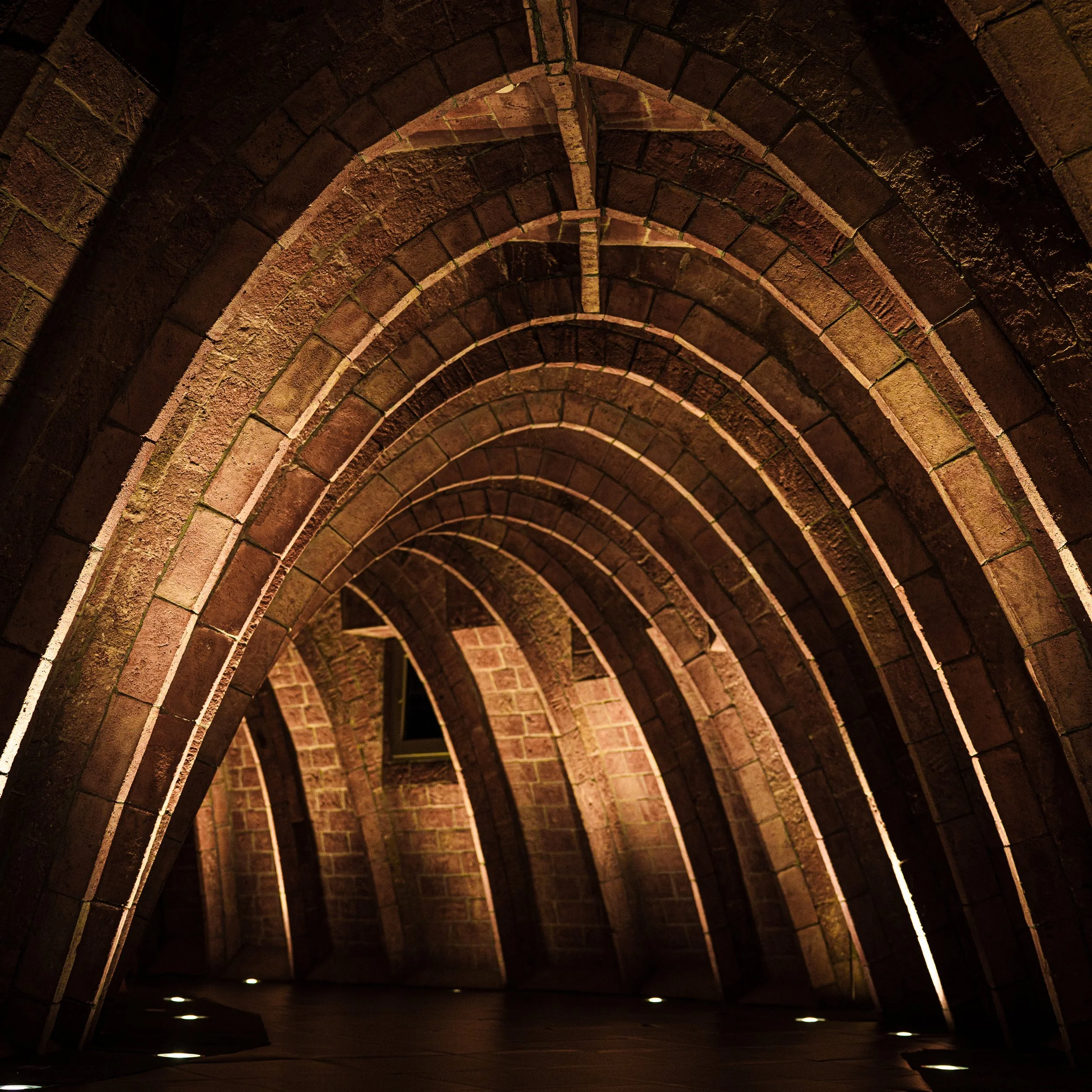 A brick archway ceiling with curved arches and small lights on the floor illuminating the space