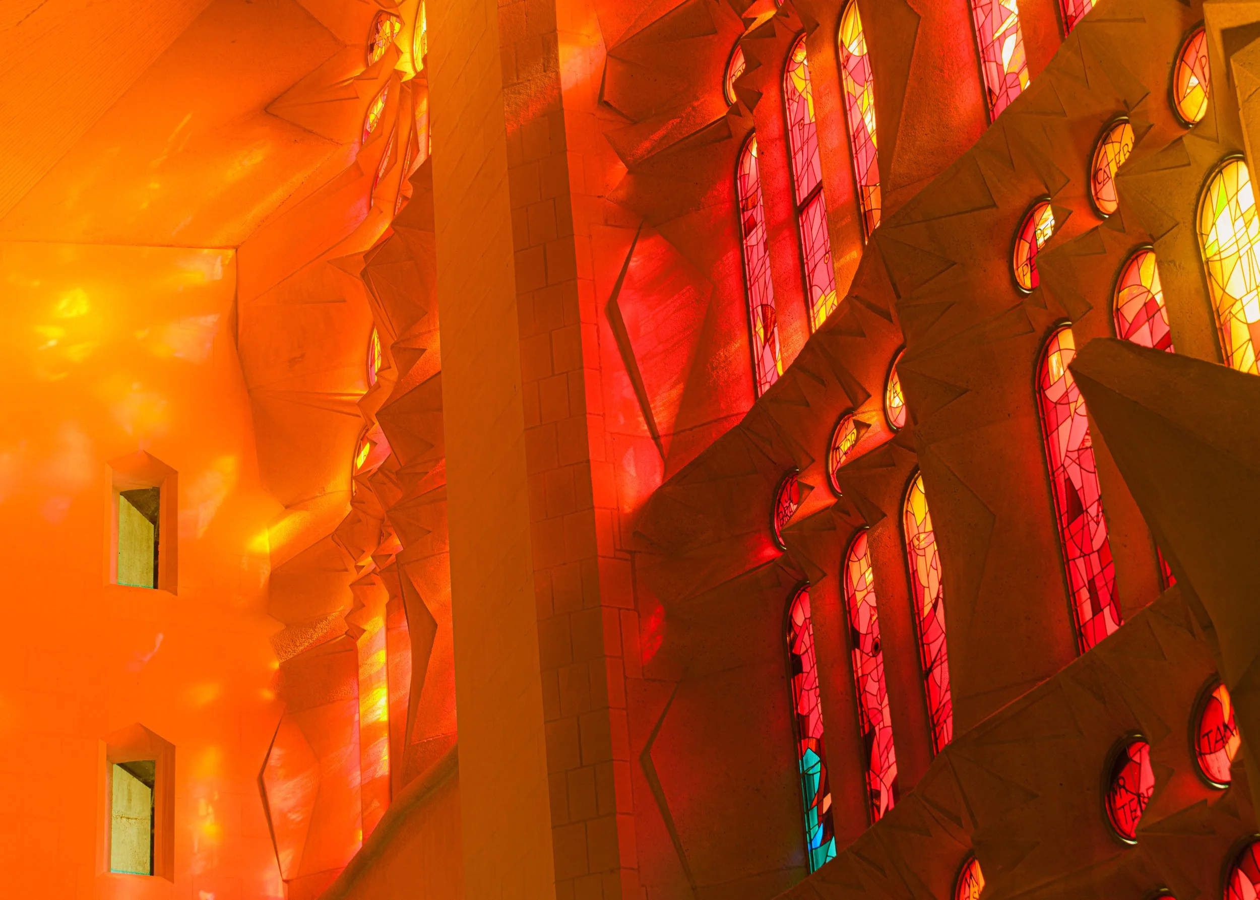 Interior of a church with stained glass windows and stone walls illuminated by orange and red lighting.
