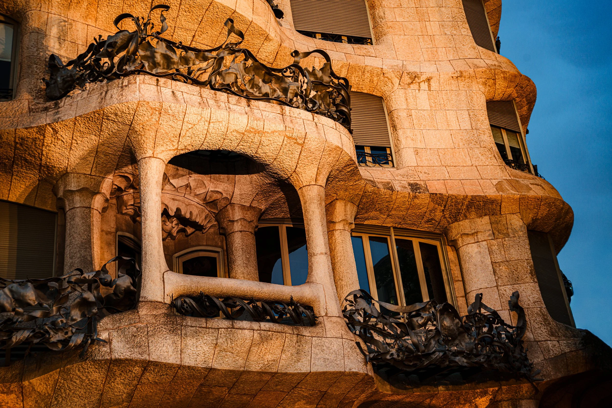 Close-up photo of a building with ornate stone balconies featuring intricate wrought iron railings, taken during sunset.