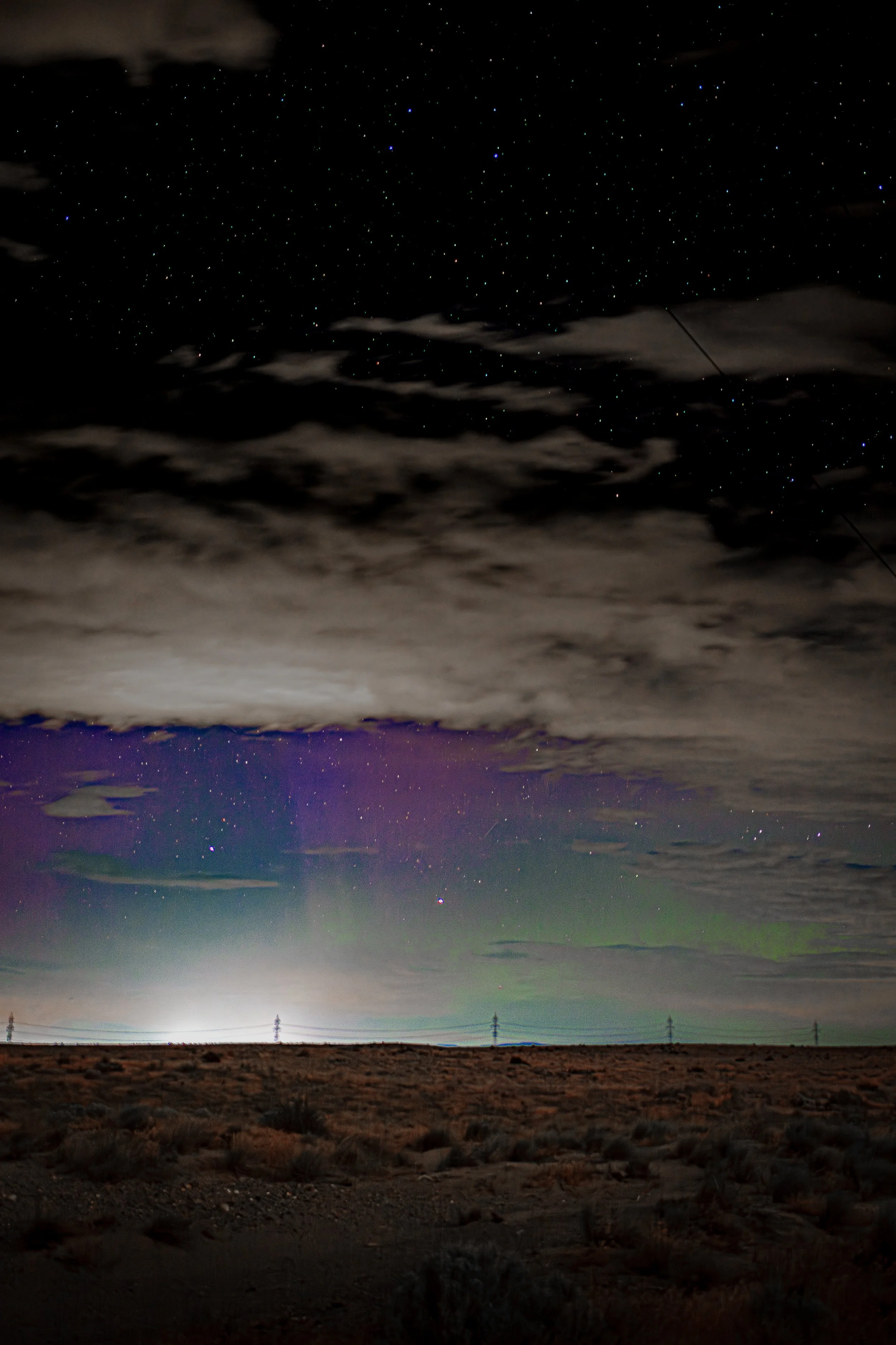 Faint green and purple aurora color appears beneath broken clouds and stars above dark Eastern Washington scrubland.
