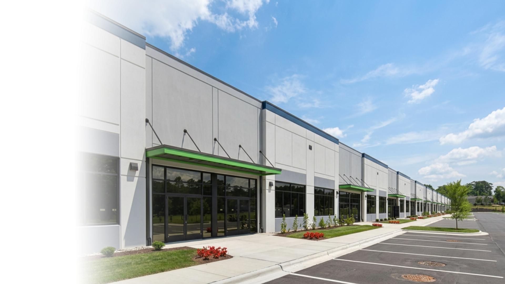 Modern commercial building with large glass windows, green awnings, and a parking lot under a blue sky with scattered clouds.