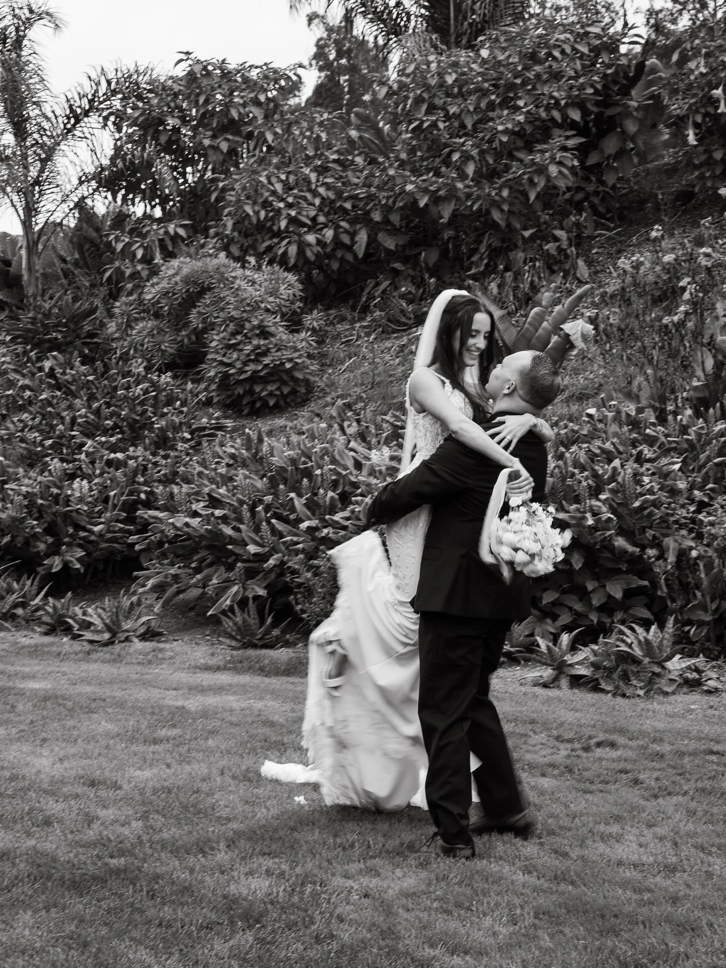 Getting married a man is holding a woman spinning her in a wedding dress with flowers in her hand.