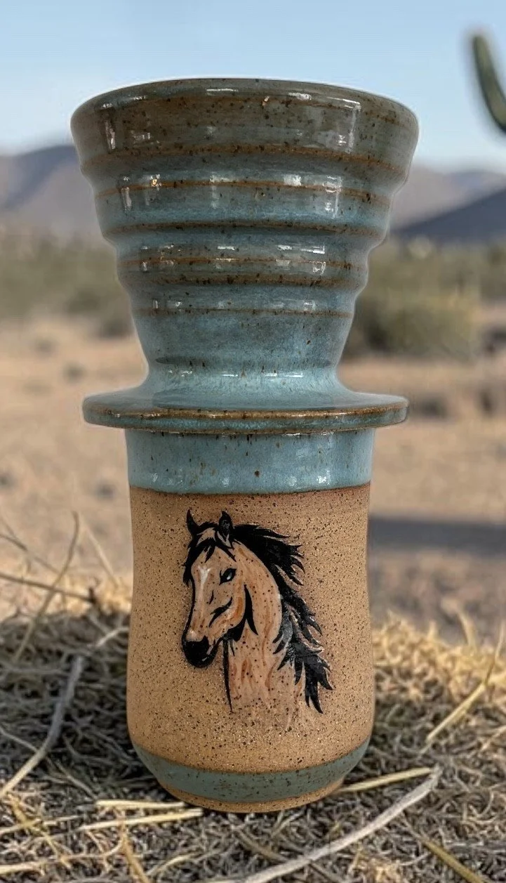 A ceramic mug with a horse illustration, situated in a desert landscape with mountains in the background.