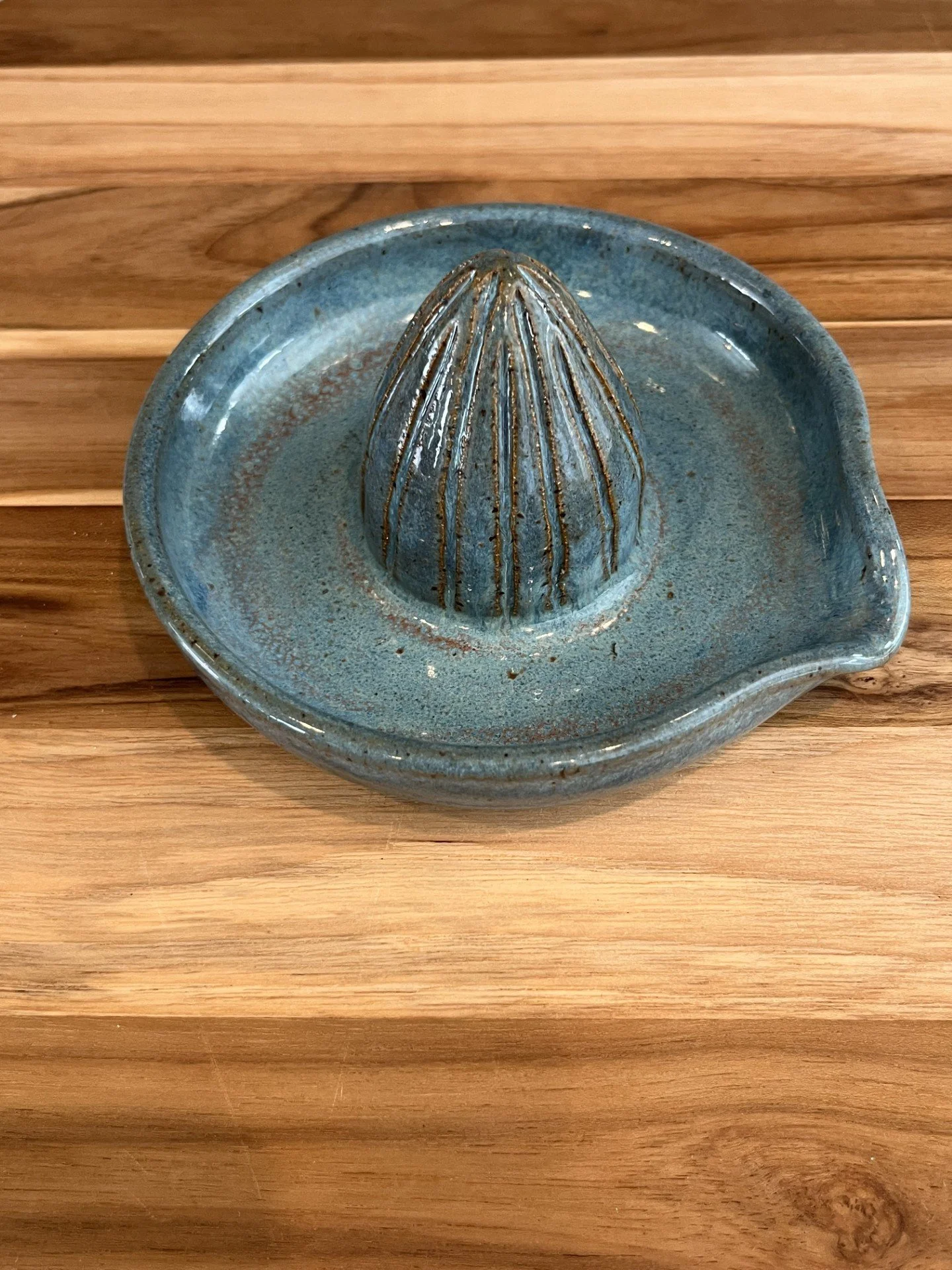 A vintage-style blue-green ceramic citrus juicer with a ridged cone in the center, placed on a wooden table.