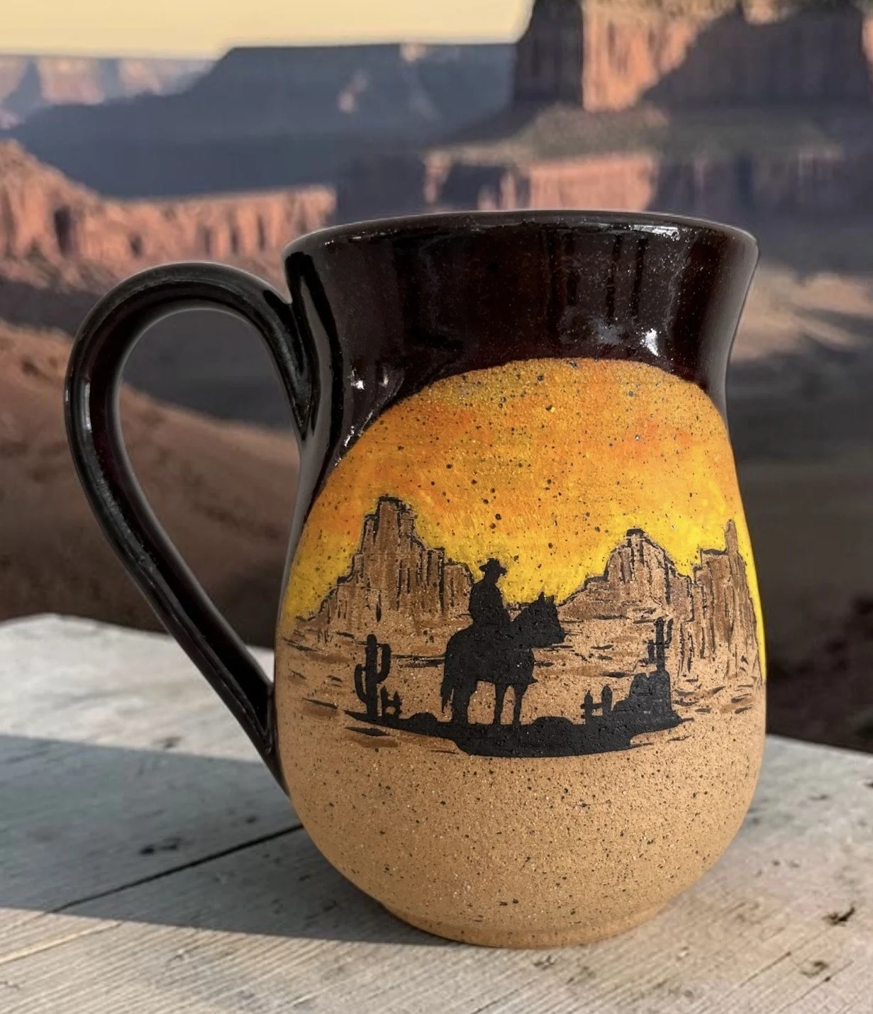 Handmade ceramic mug featuring a cowboy on horseback against a desert landscape with cacti and mountains.
