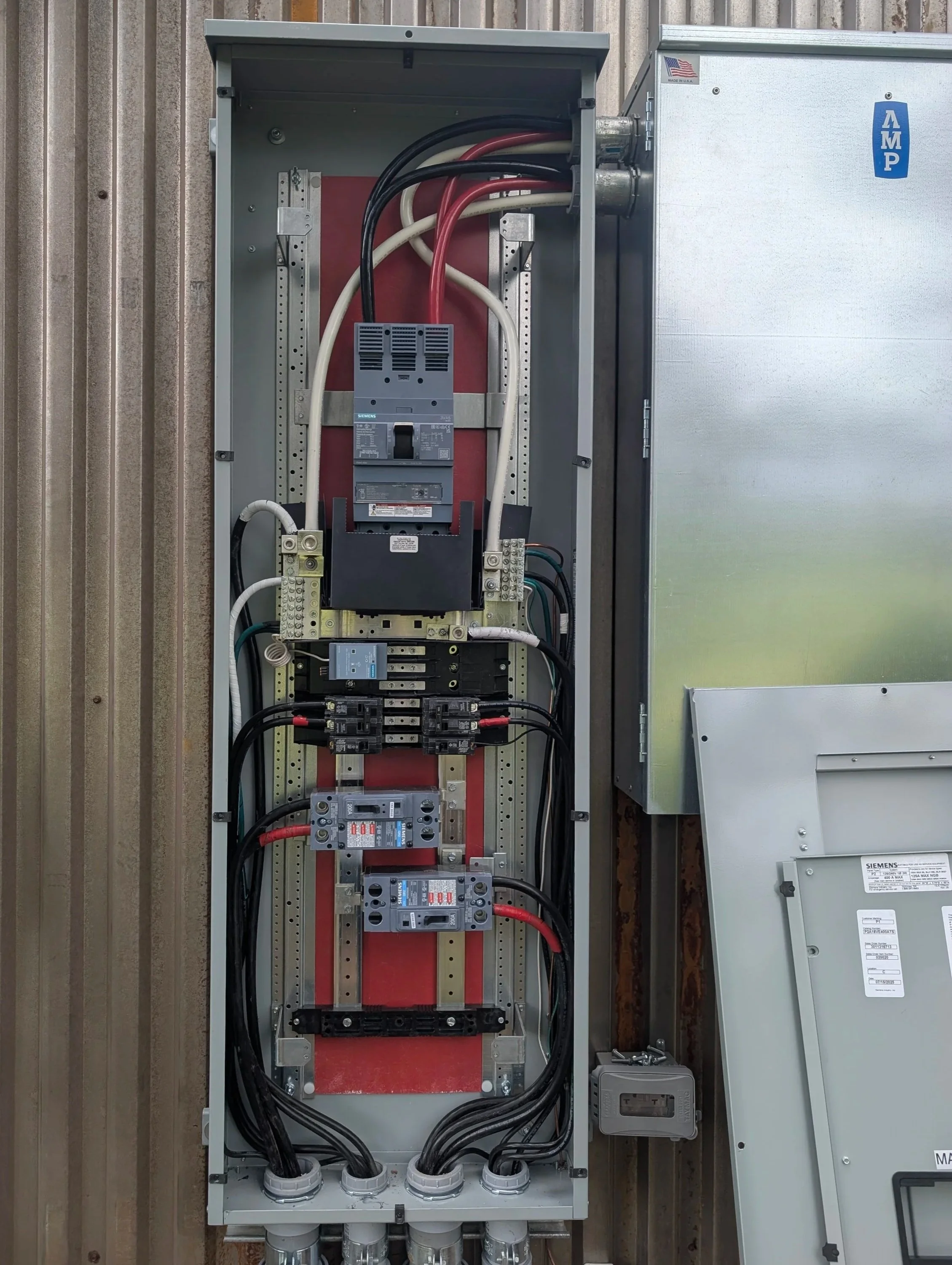 Electrical panel with various wires and circuit breakers inside a metal box, mounted on a wall.