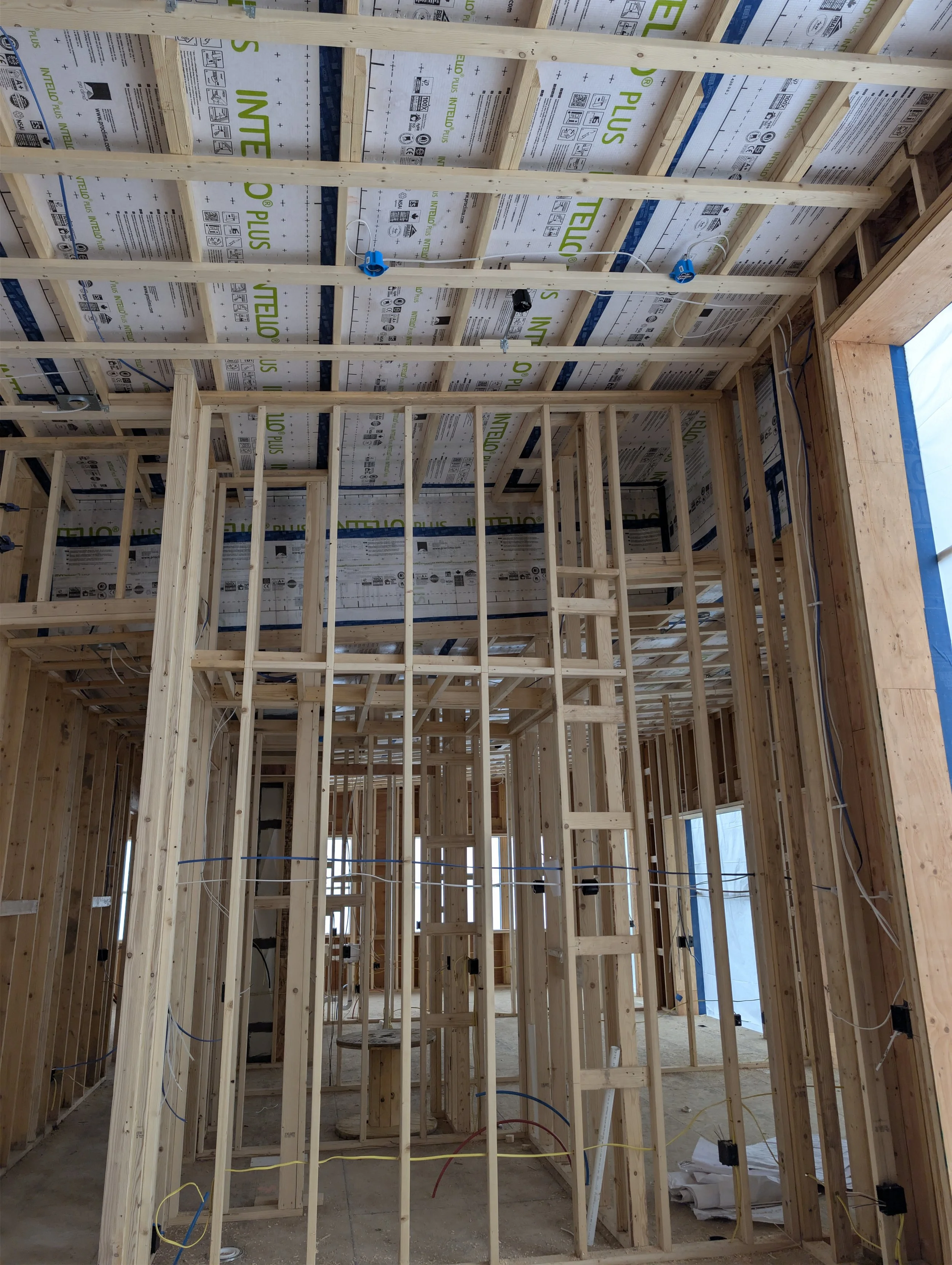Interior of a house under construction with exposed wooden studs, wiring, and insulation on the ceiling. New Construction, and remodel wiring.