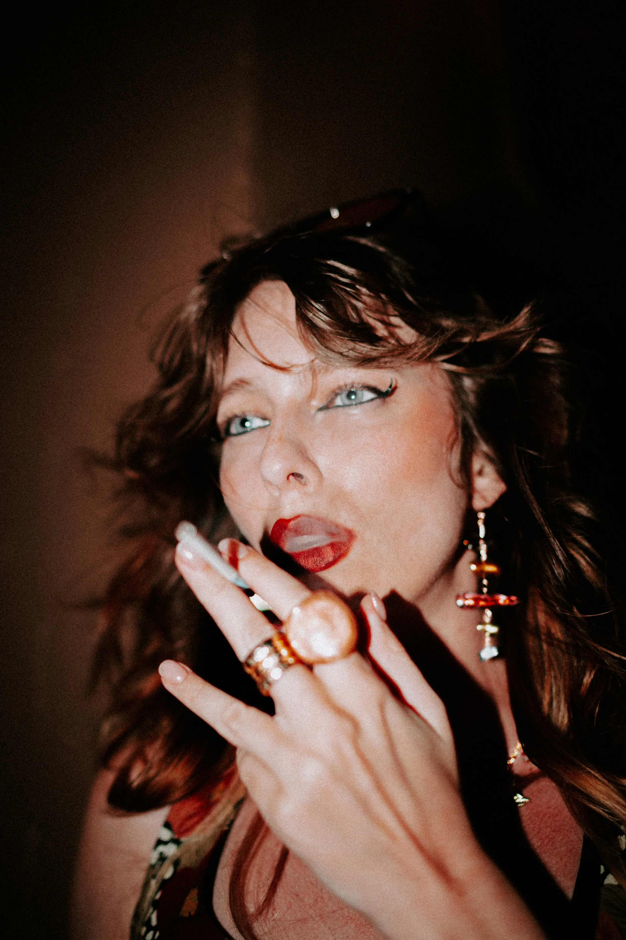 A woman with dark, curly hair and makeup smoking a cigarette