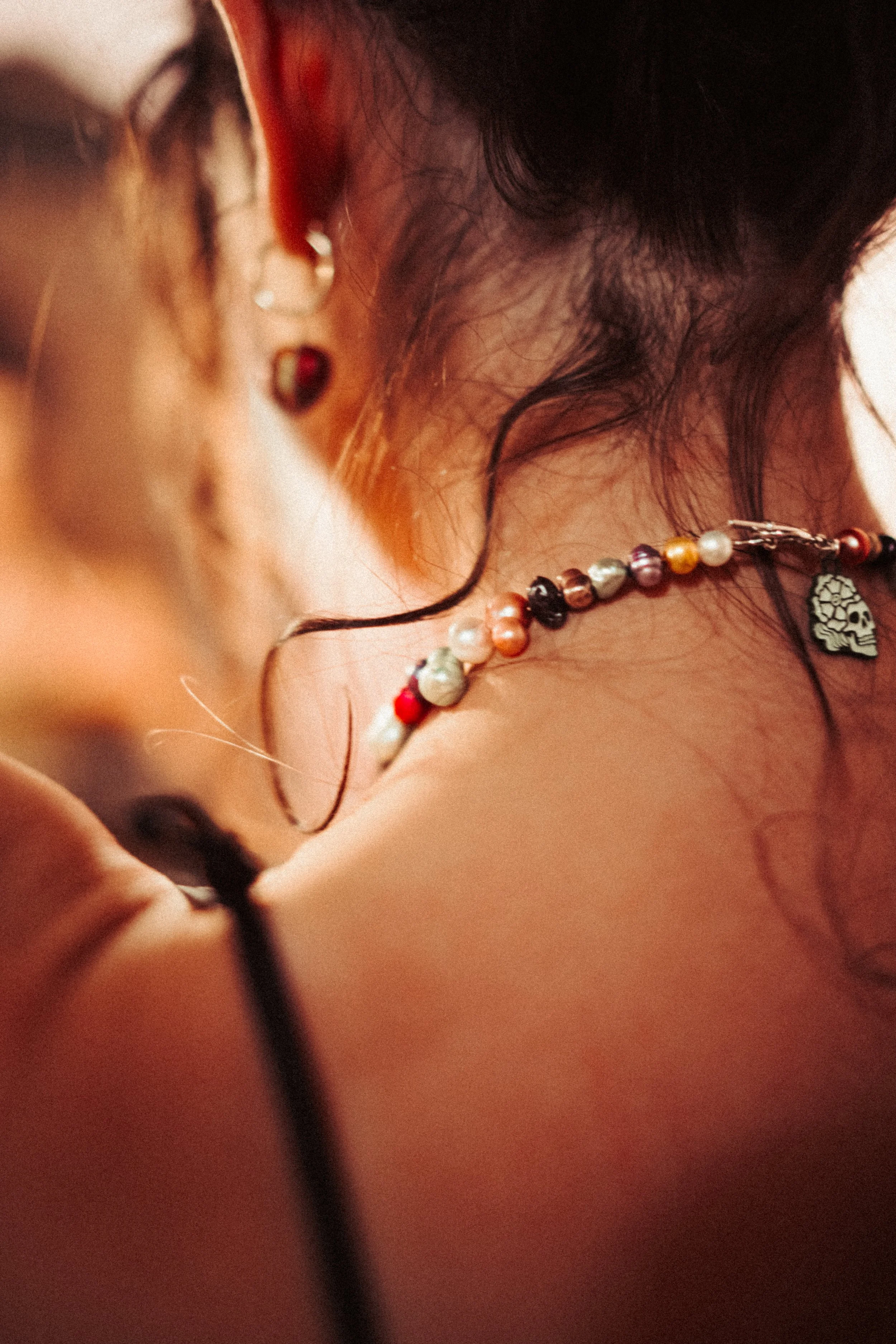 Close-up of a woman's face, showing her wearing glasses, a beaded necklace, and earrings, with dark hair and a warm background.