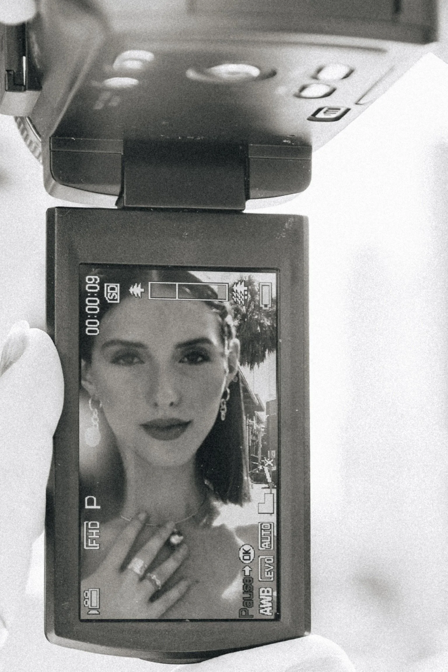 Black and white photo of a digital camera's LCD screen showing a portrait of a woman with dark lipstick and curly hair, with camera settings visible around the edges.
