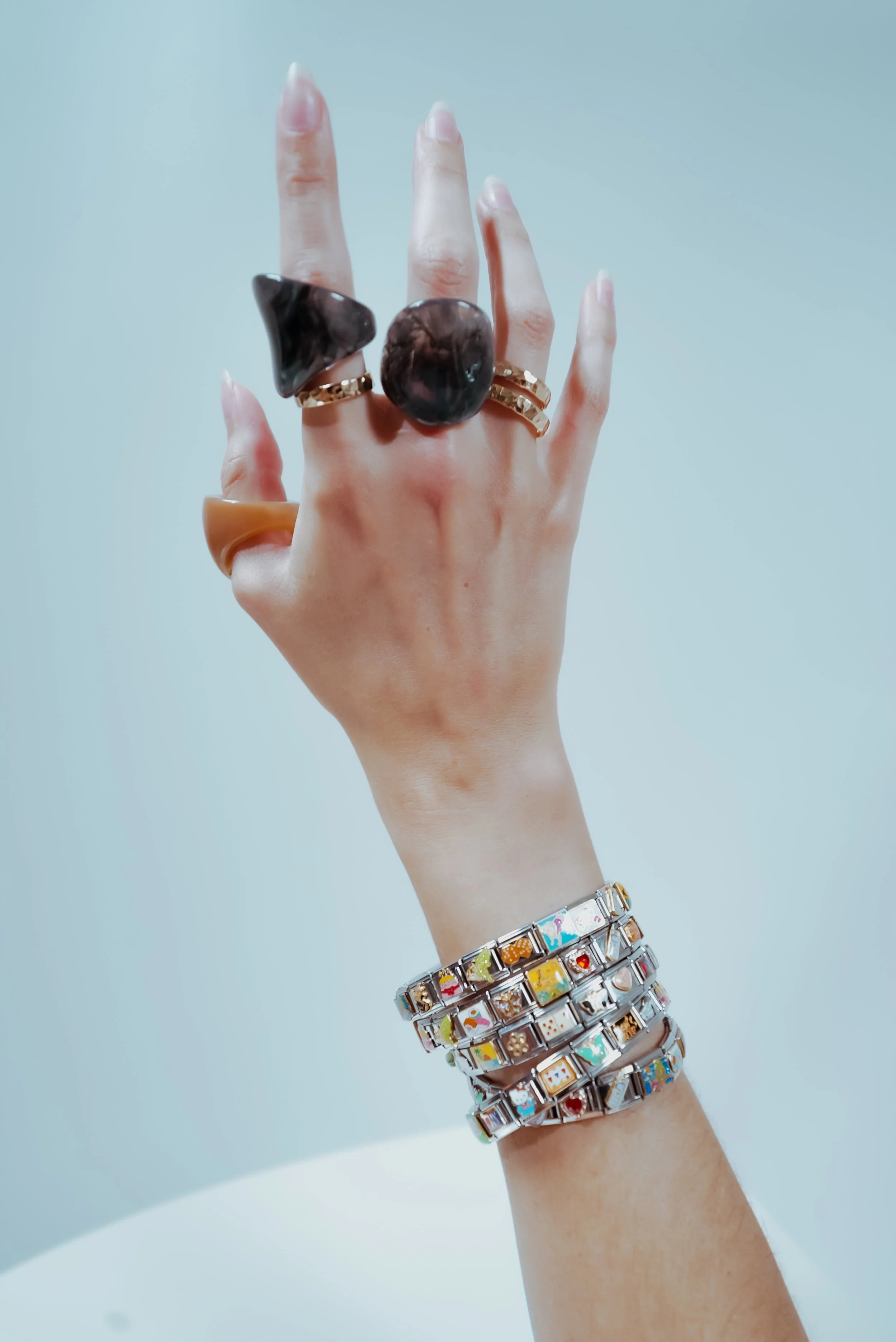 A hand displaying multiple jewelry rings and bracelets against a plain background.