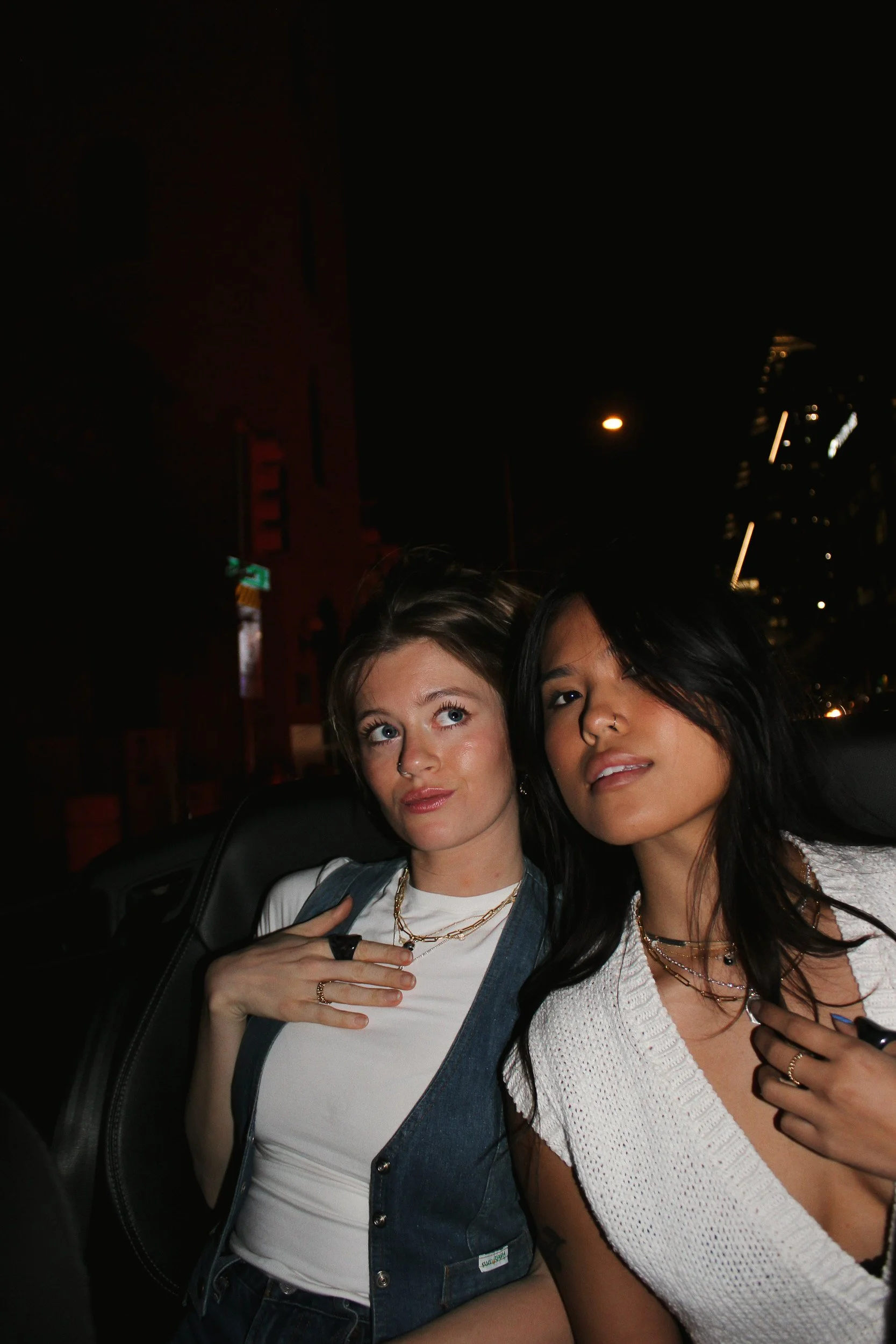 Two women standing close together at night, in front of city buildings with lights, posing for a photo.