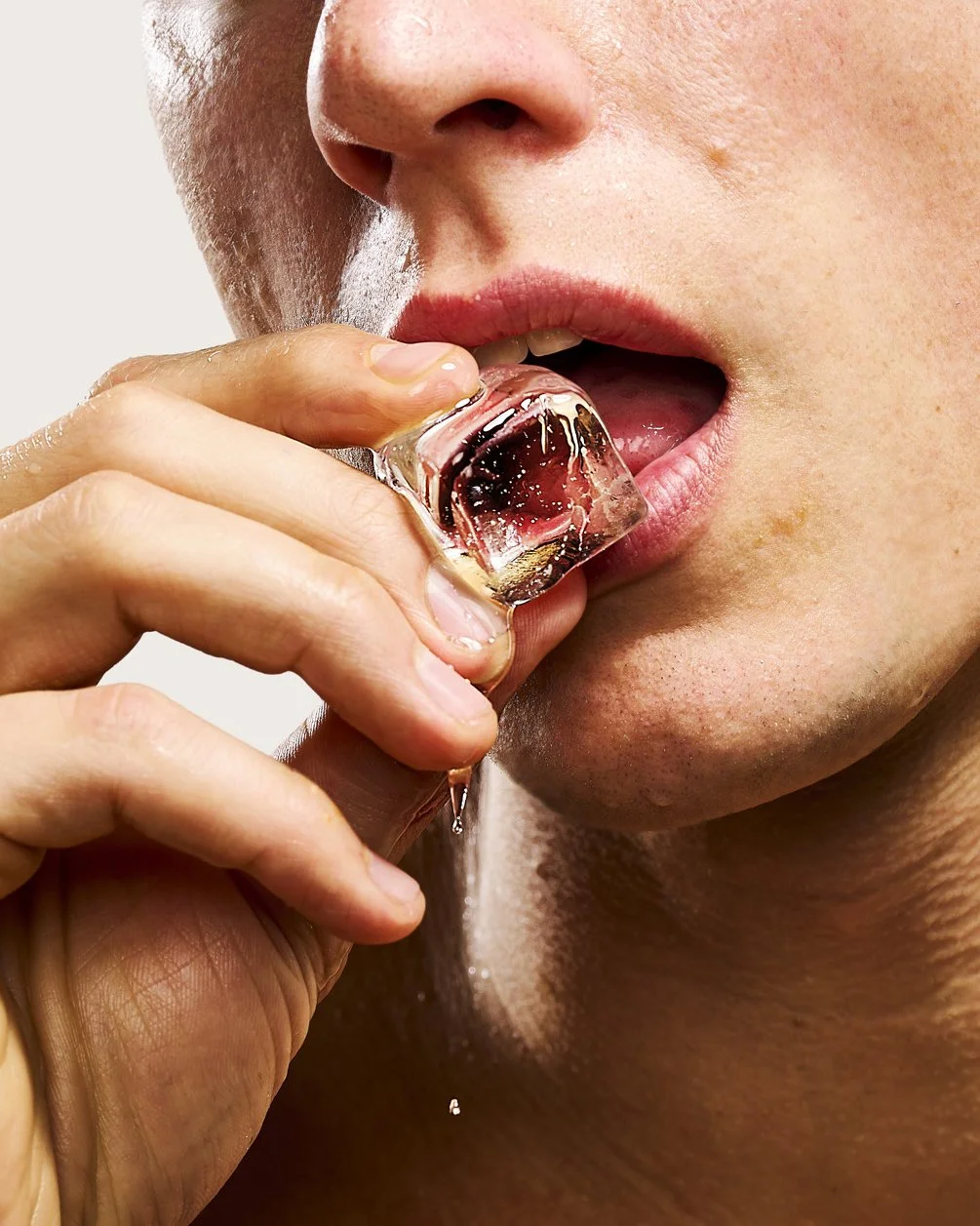 Close-up of a person about to lick an ice cube with a mouth slightly open, showing lips and part of nose and chin.