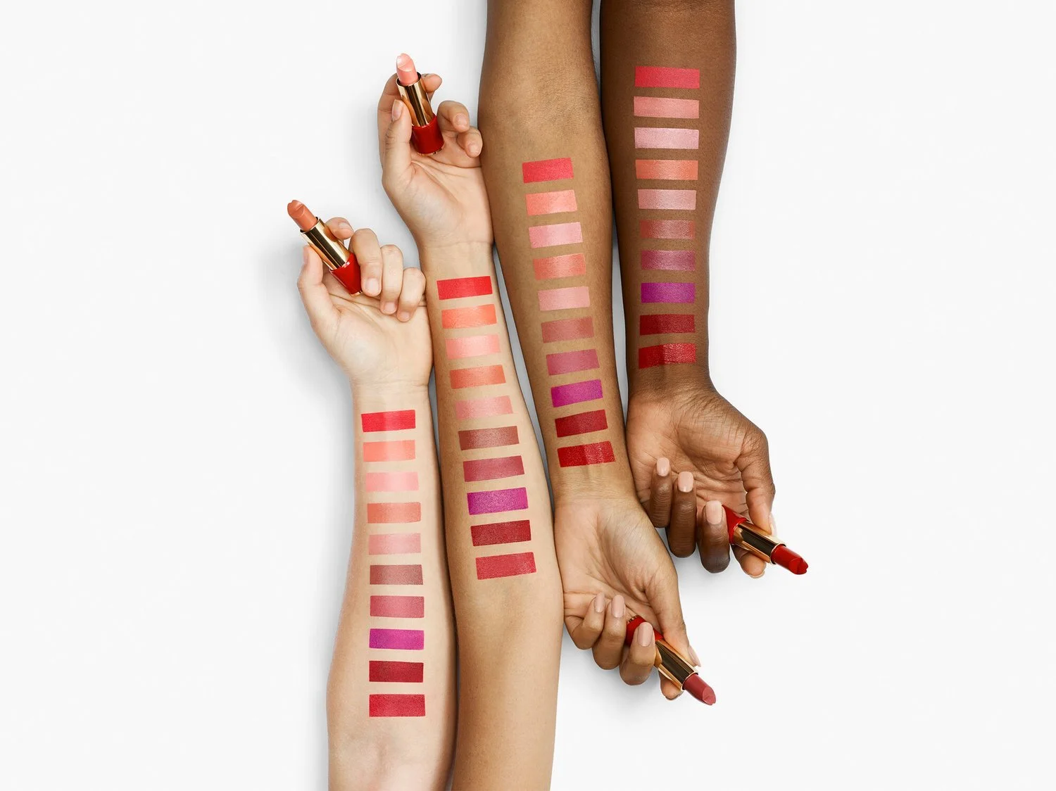 Multiple arms with various skin tones holding red lipstick, each arm with swatches of different lipstick shades on the forearm.