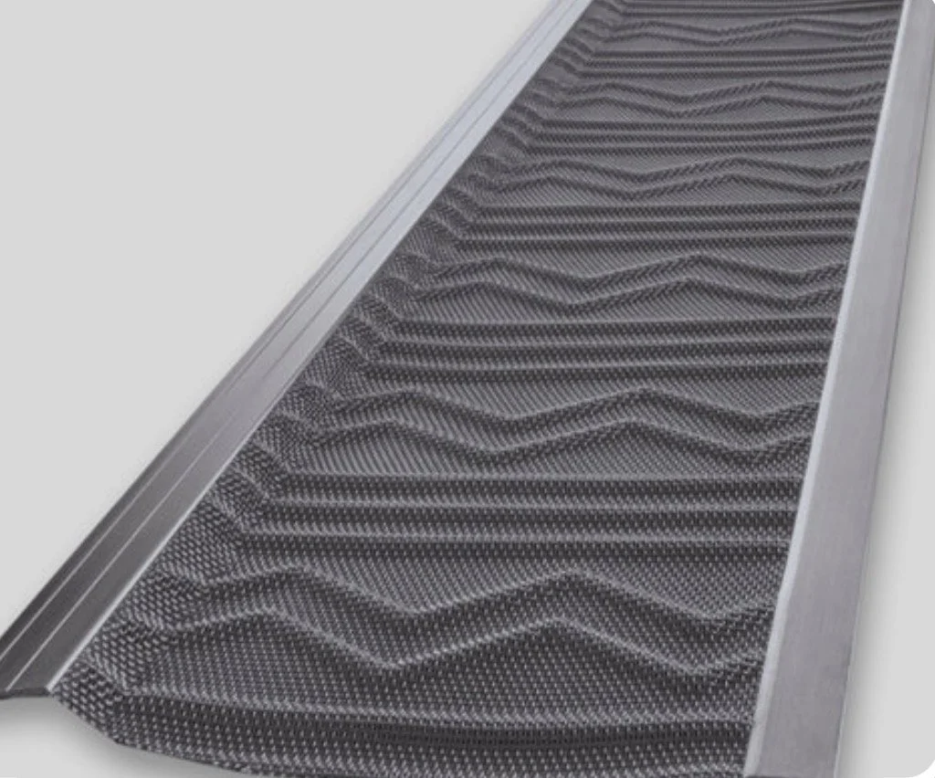 Close-up of a black rubber doormat with textured wave pattern and metal frame.