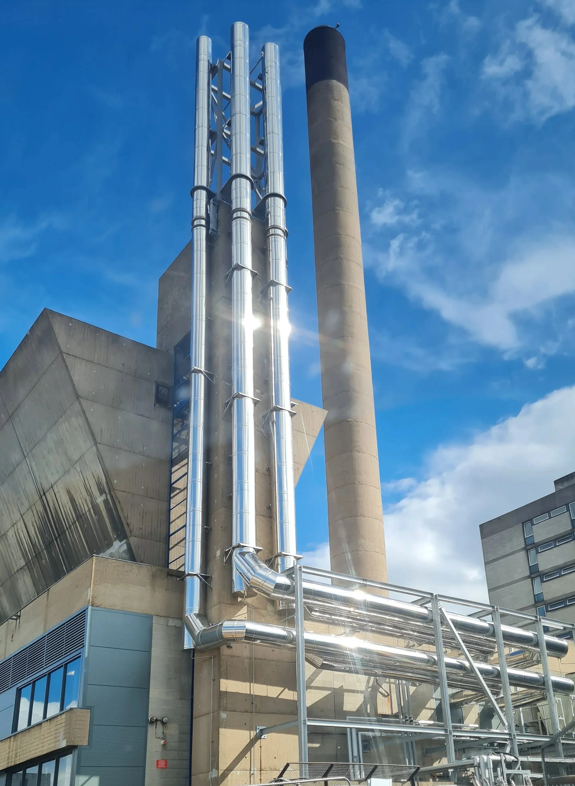 Four twin‑wall stainless steel flue risers installed at Hull Royal Infirmary, running vertically then horizontally into the plant room.